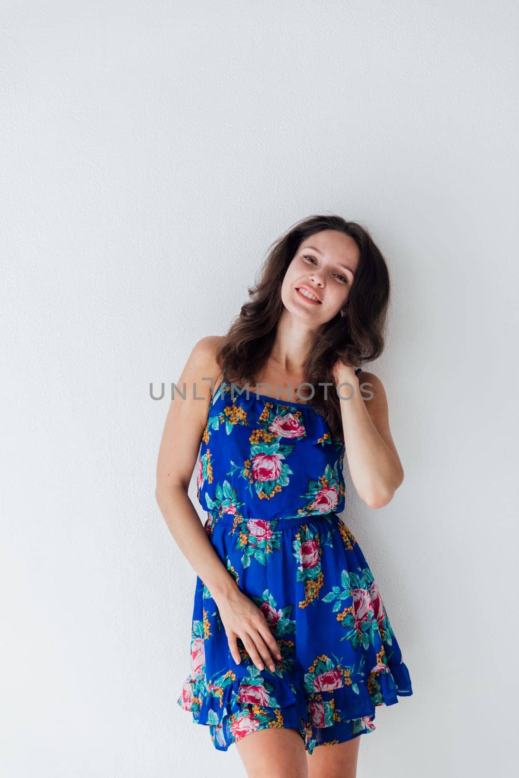 brunette woman in a blue floral dress against a white wall by Simakov
