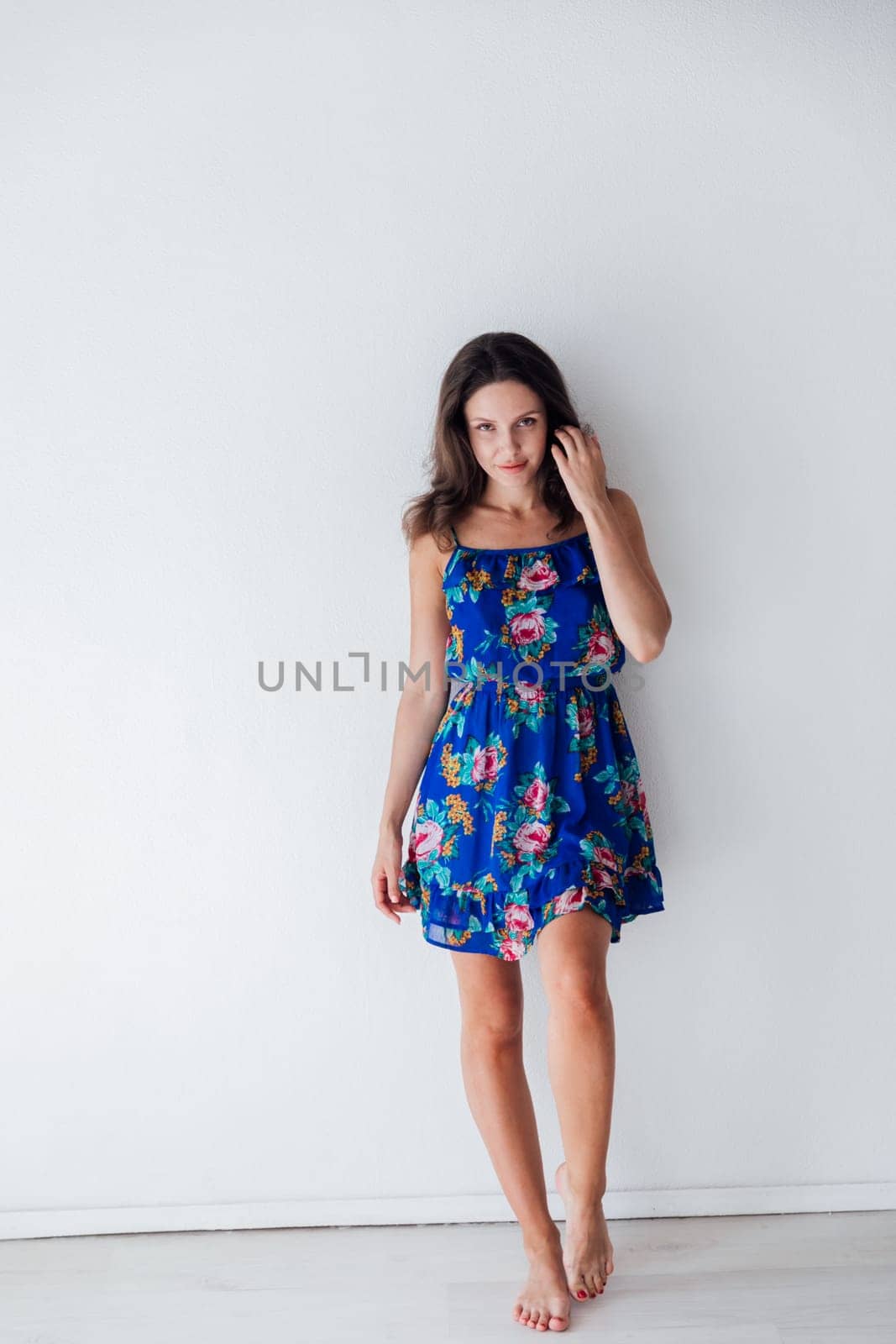 brunette woman in a blue floral dress against a white wall by Simakov
