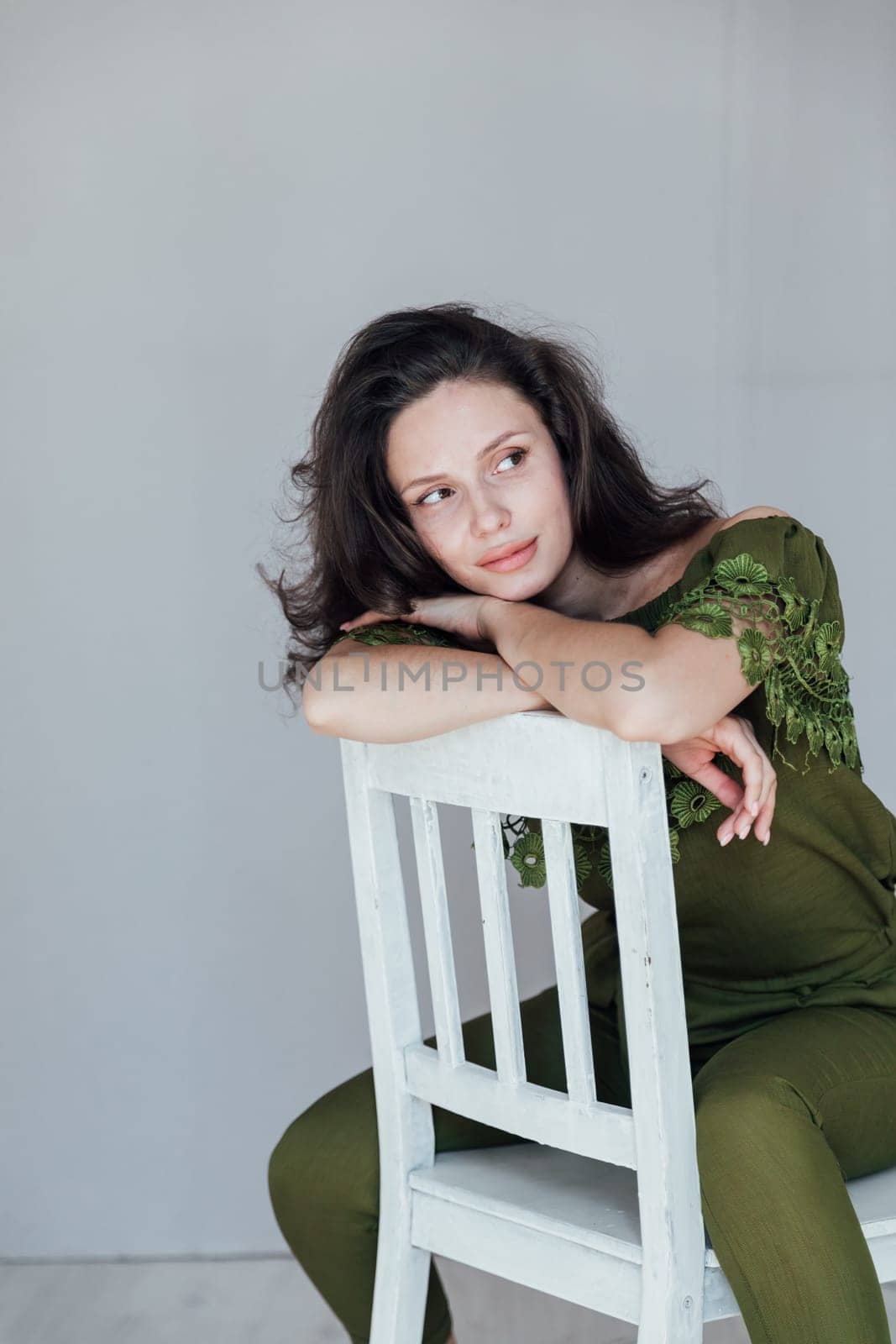 fashionable woman sits on a white chair and poses on a gray background
