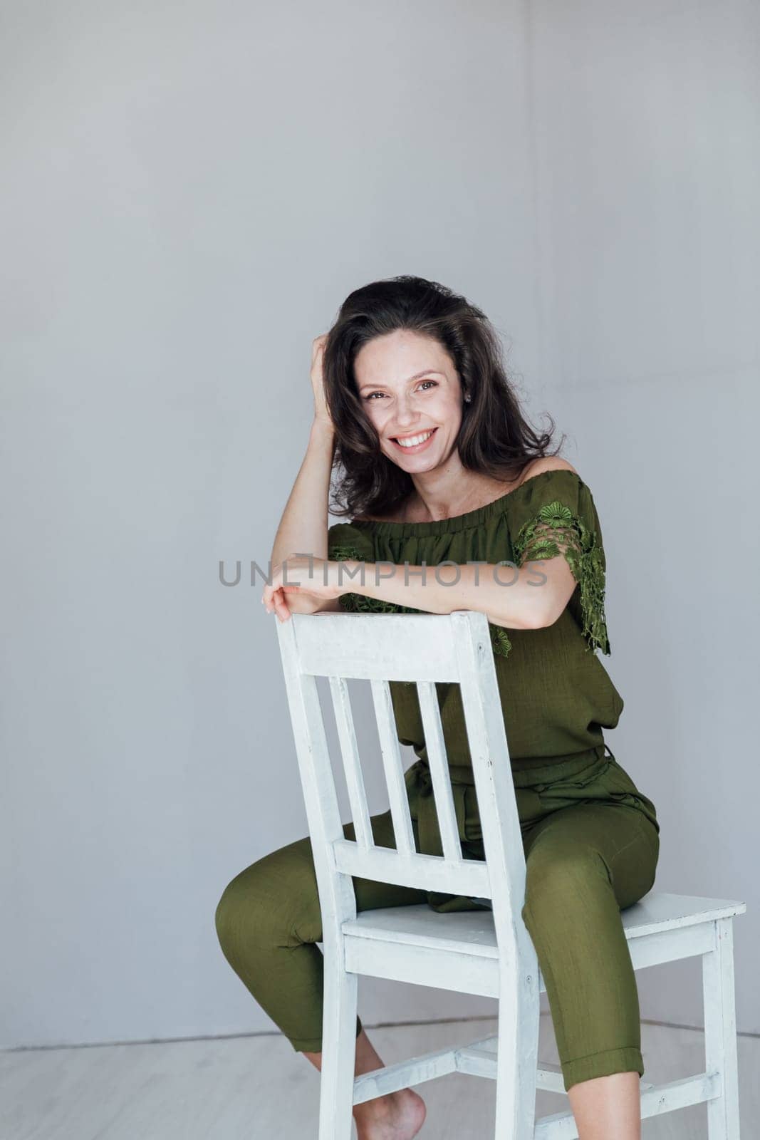 fashionable woman sits on a white chair and poses on a gray background
