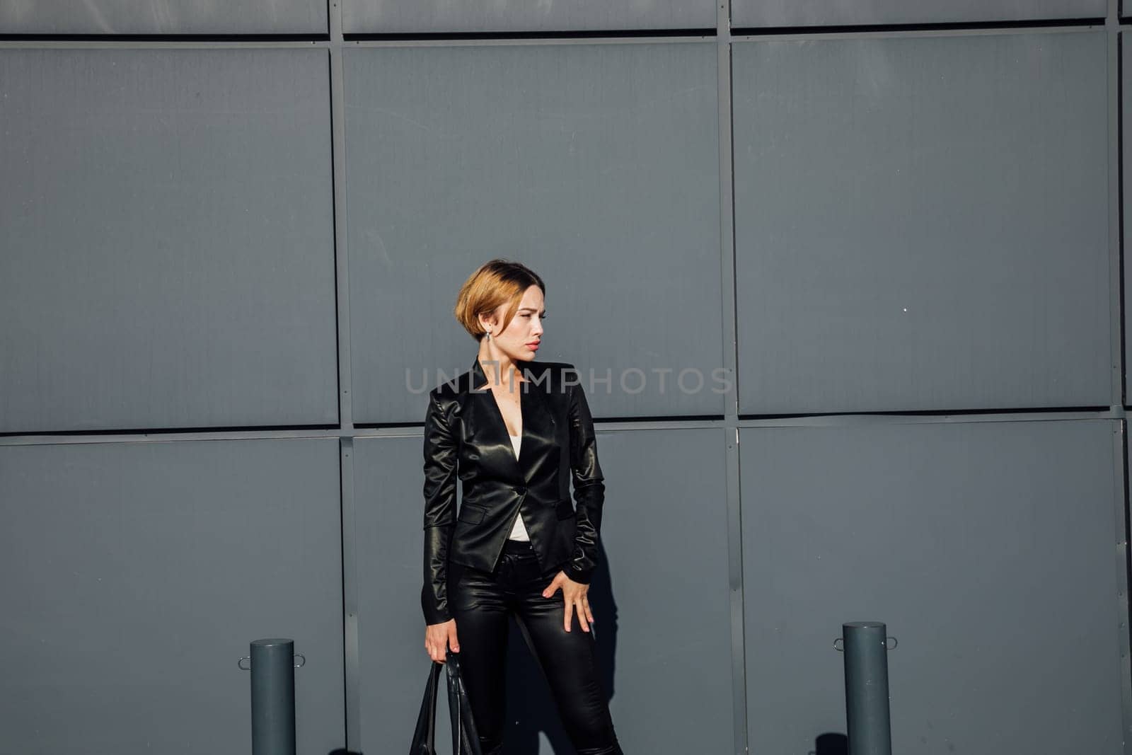 fashionable woman in leather black clothes stands against a graphic wall