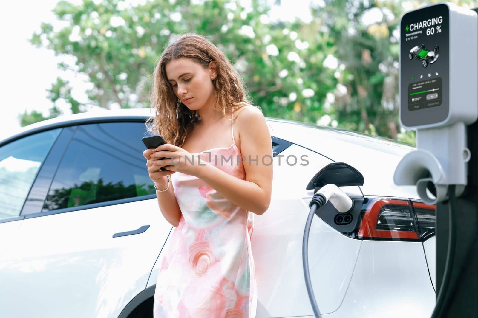 Modern eco woman recharge EV car with smartphone. Synchronos by biancoblue