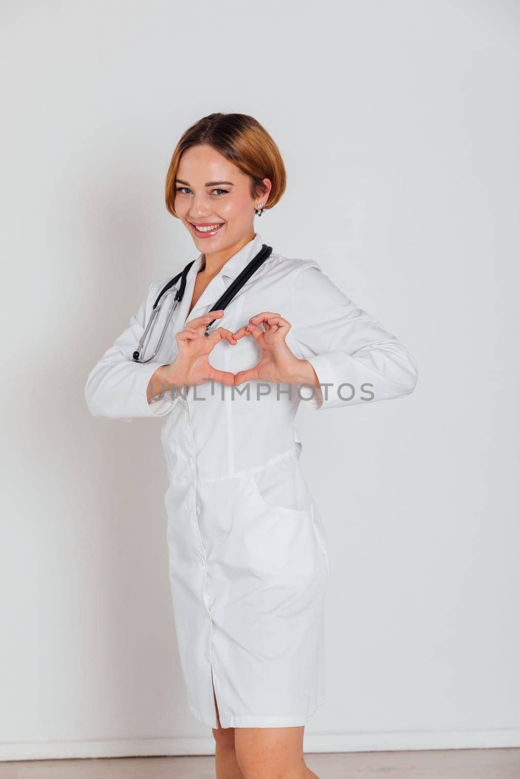 a woman doctor in white coat with phonendoscope shows heart