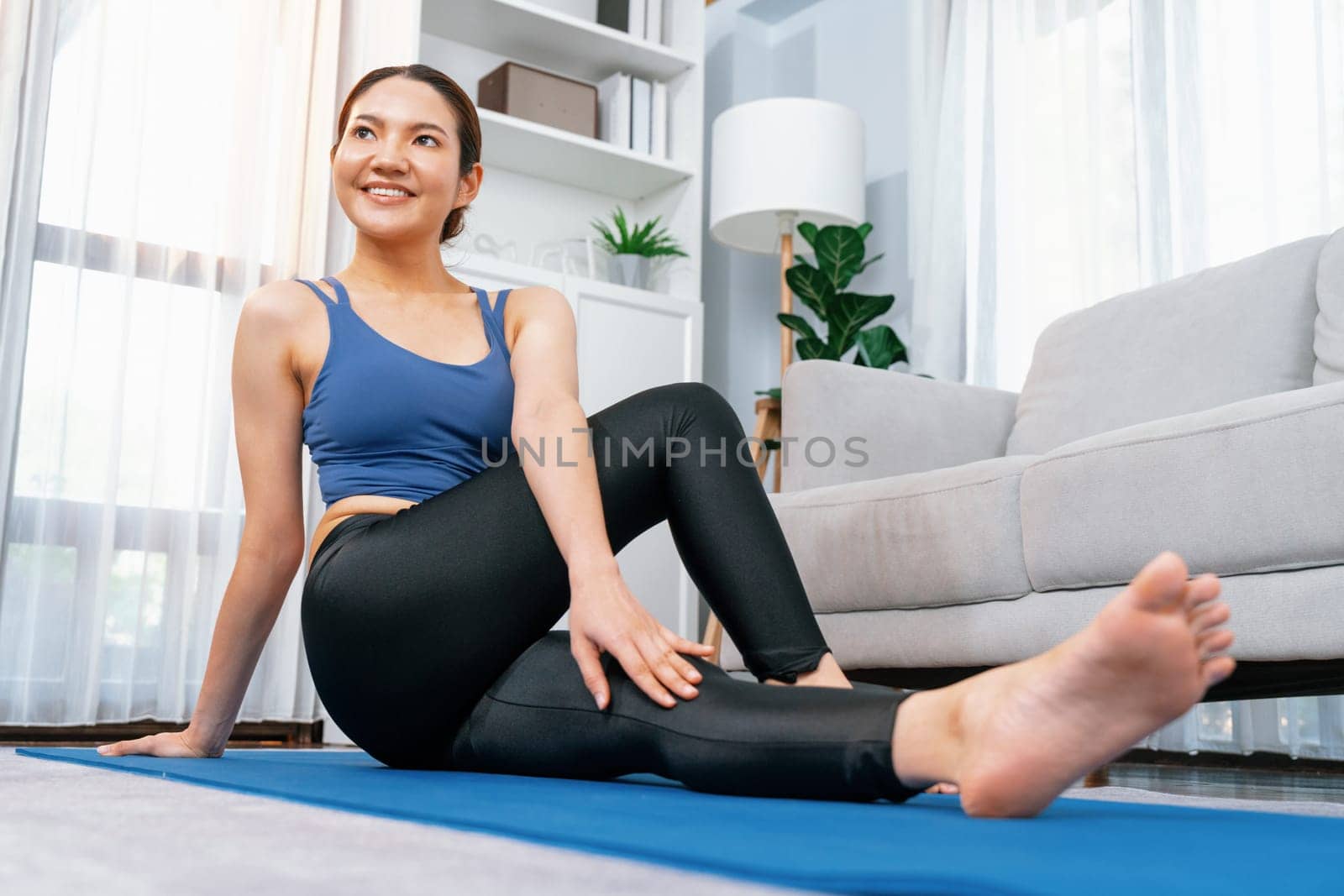 Asian woman in sportswear doing yoga exercise on fitness mat as her home workout training routine. Healthy body care and calm meditation in yoga lifestyle with comfortable and relaxation. Vigorous