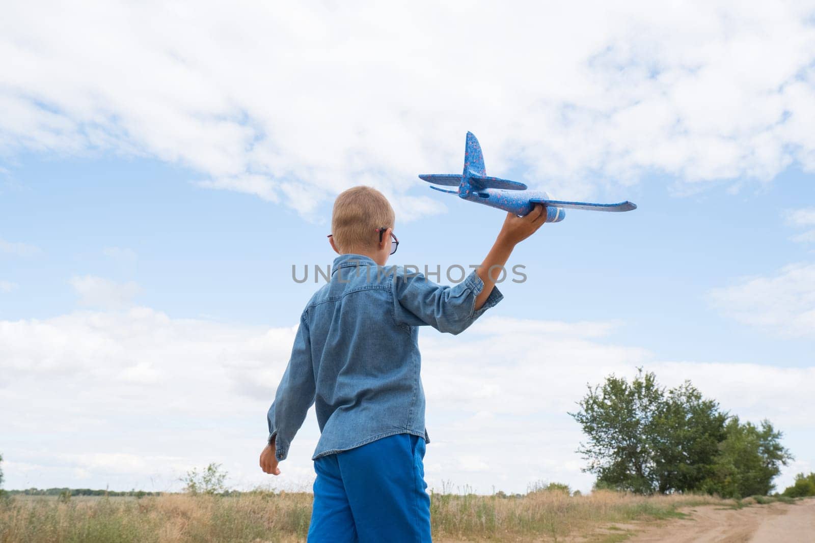 Portrait of a happy child playing with a toy airplane against a blue sky in an open field.