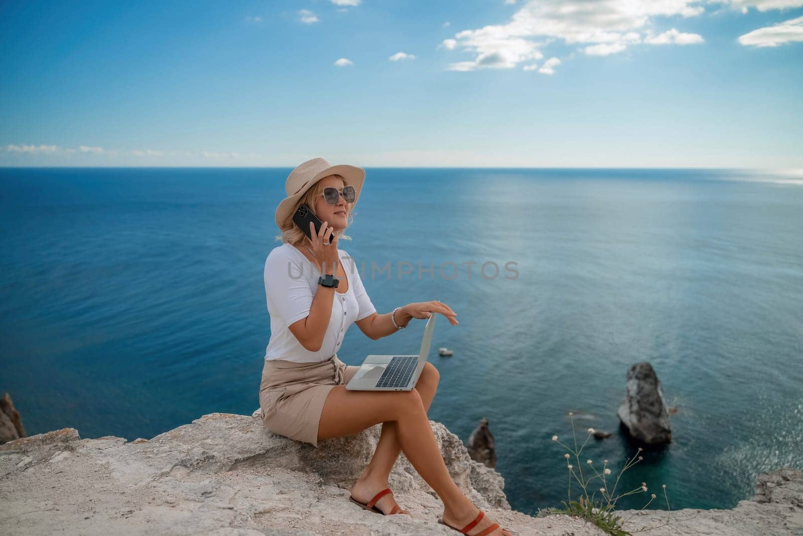 Freelance women sea working on the computer. Good looking middle aged woman typing on a laptop keyboard outdoors with a beautiful sea view. The concept of remote work