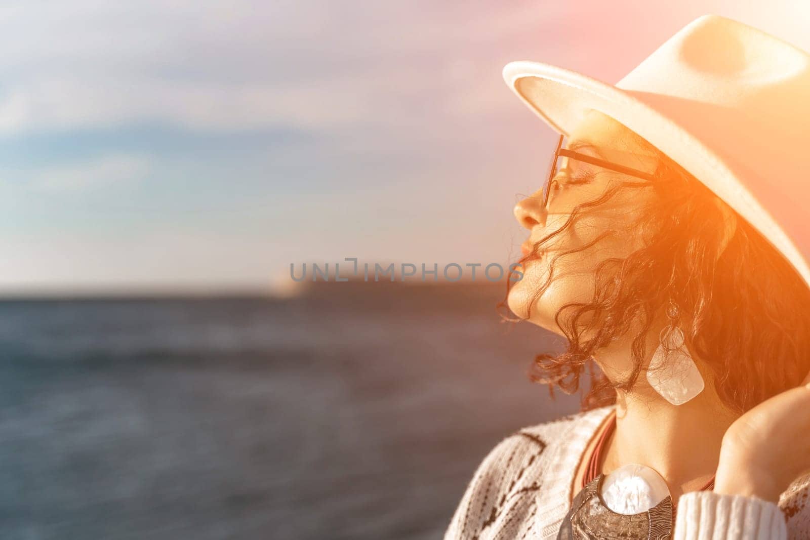 Portrait of a curly haired woman in a white hat and glasses on the background of the sea