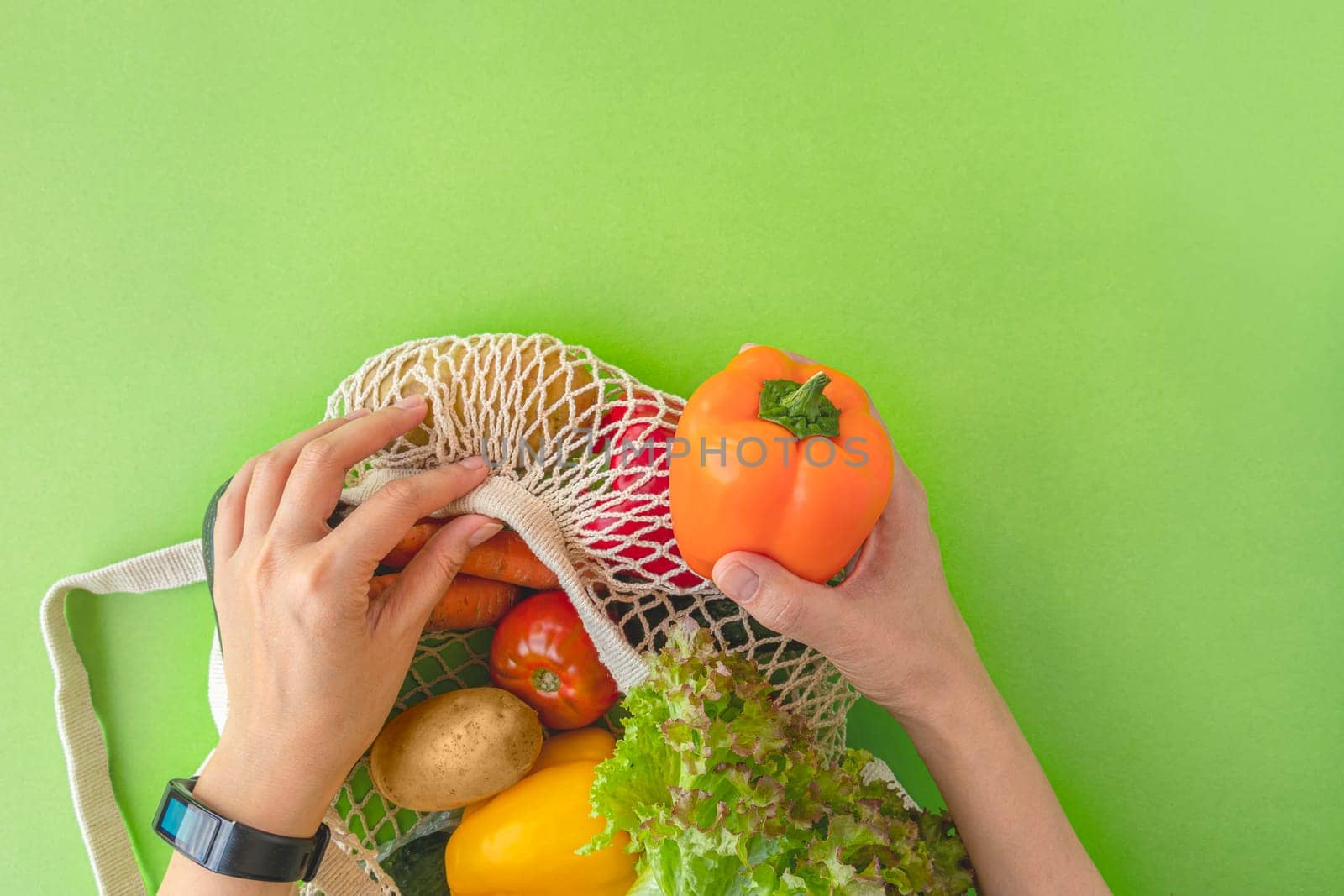 top view of woman's hands taking vegetables out of eco-bag. tomatoes, cucumbers, bell peppers and lettuce in reusable bag. concept of recycling, respect for nature. flat lay, copy space. soft focus by Leoschka