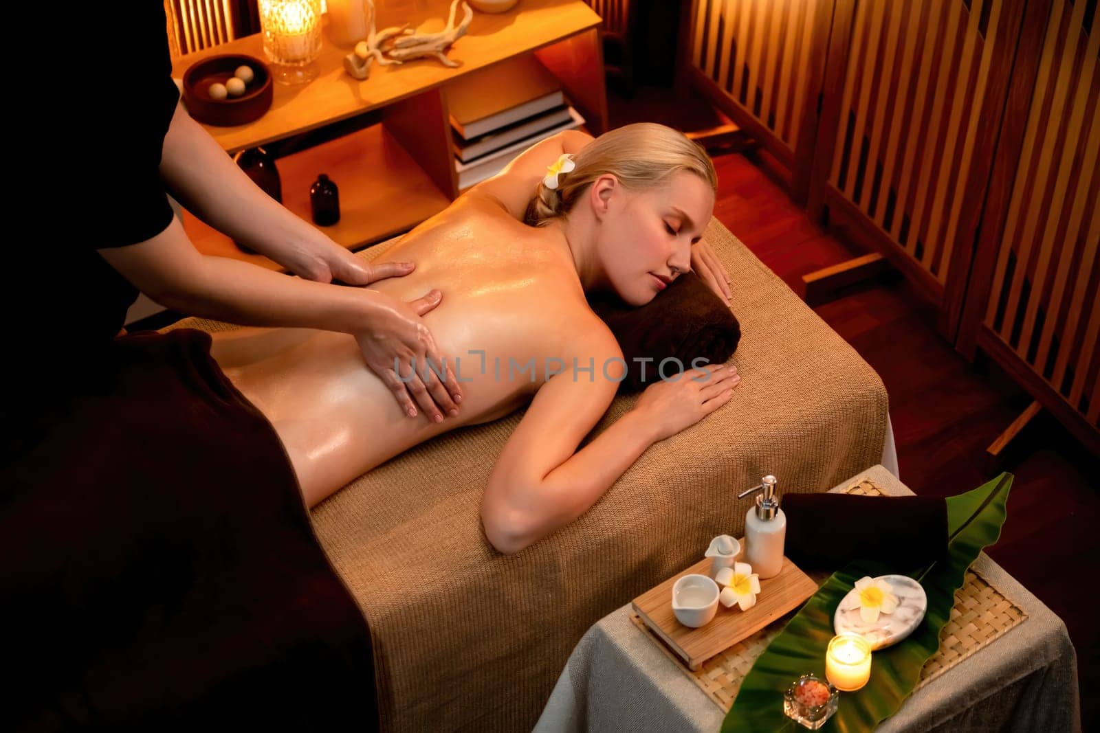 Caucasian woman customer enjoying relaxing anti-stress spa massage and pampering with beauty skin recreation leisure in warm candle lighting ambient salon spa at luxury resort or hotel. Quiescent