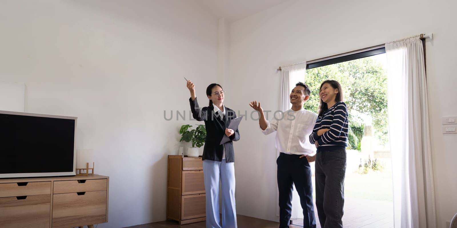 Young couple follow a real estate agent who is giving them a tour around a home, showing all the room and telling about all the advantage of living. Buying house or apartment concept.