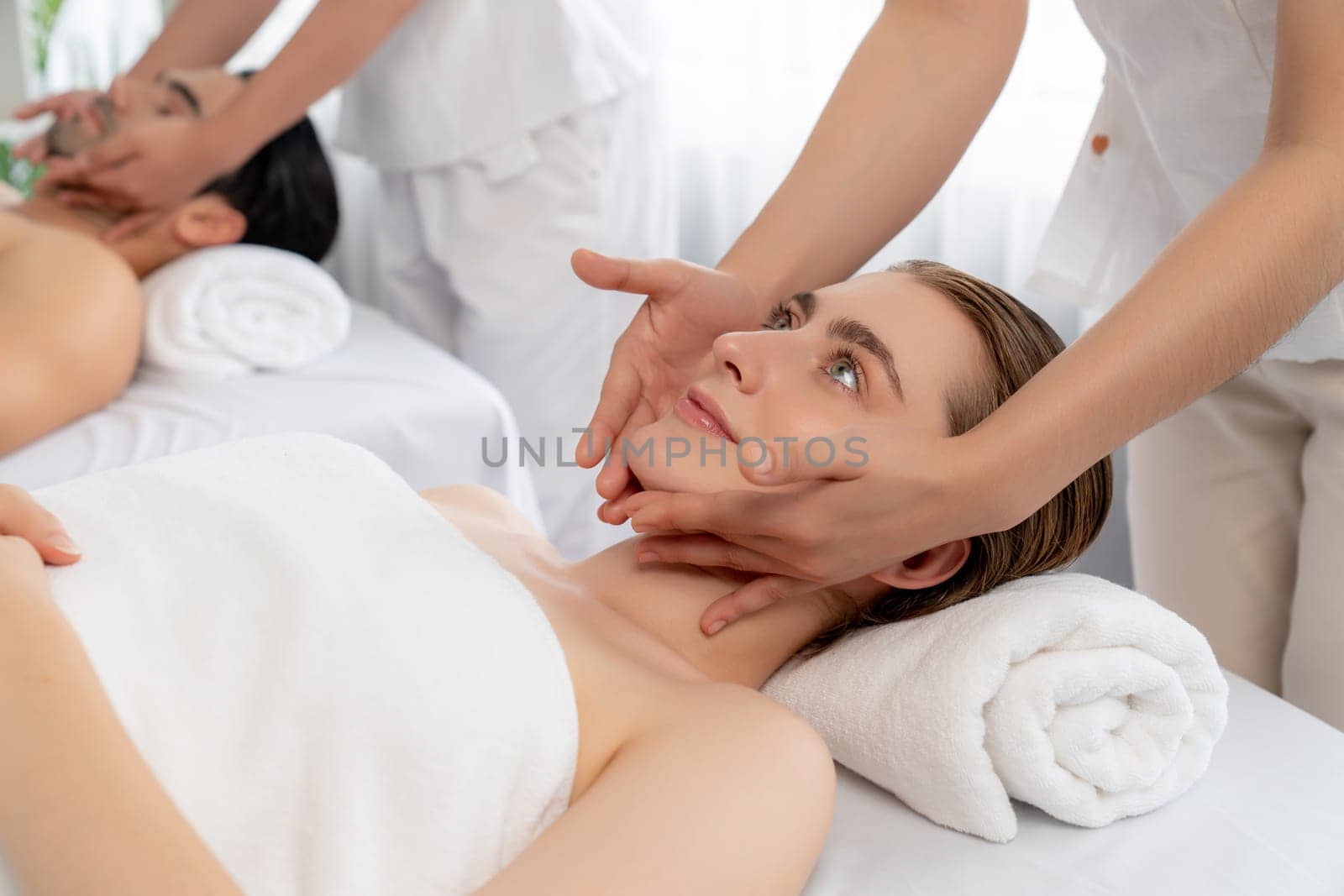 Caucasian couple enjoying relaxing anti-stress head massage and pampering facial beauty skin recreation leisure in dayspa modern light ambient at luxury resort or hotel spa salon. Quiescent