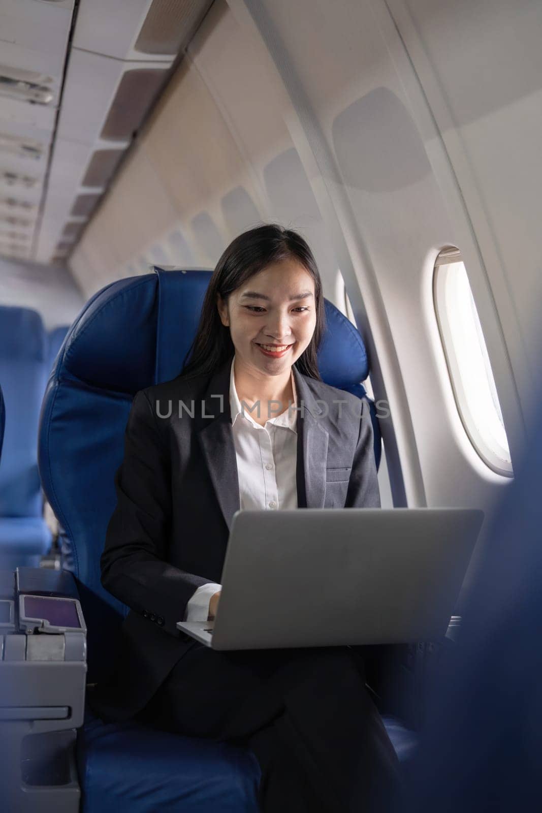Traveling and technology. Flying at first class. Pretty young Asian business woman using laptop while sitting in airplane.