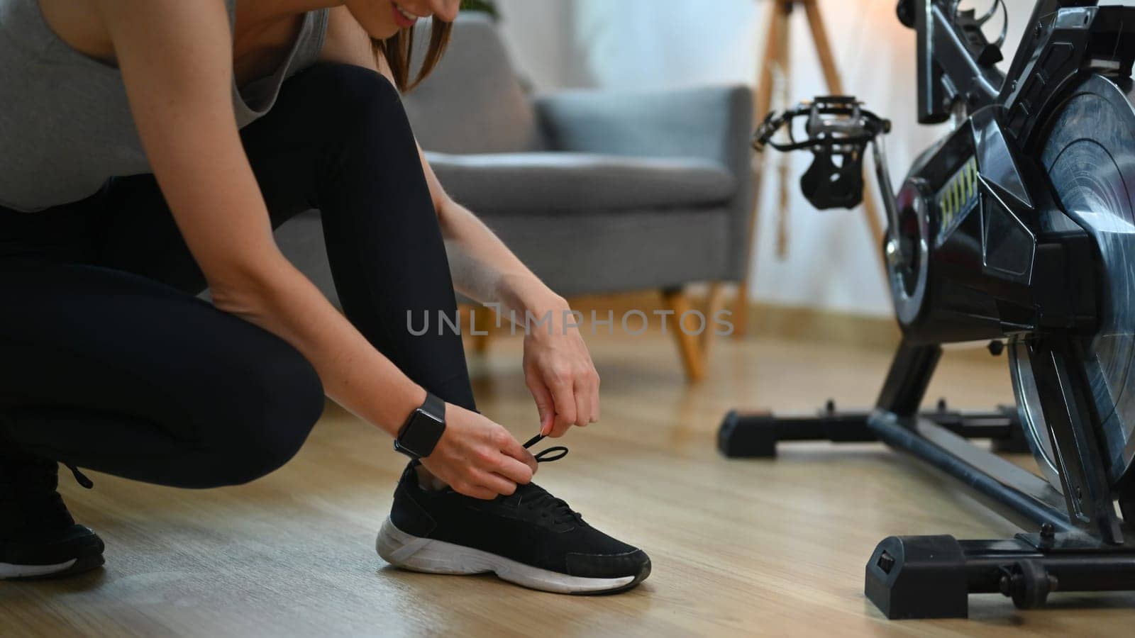 Cropped shot legs of young woman tying shoelace, preparation before home workout.