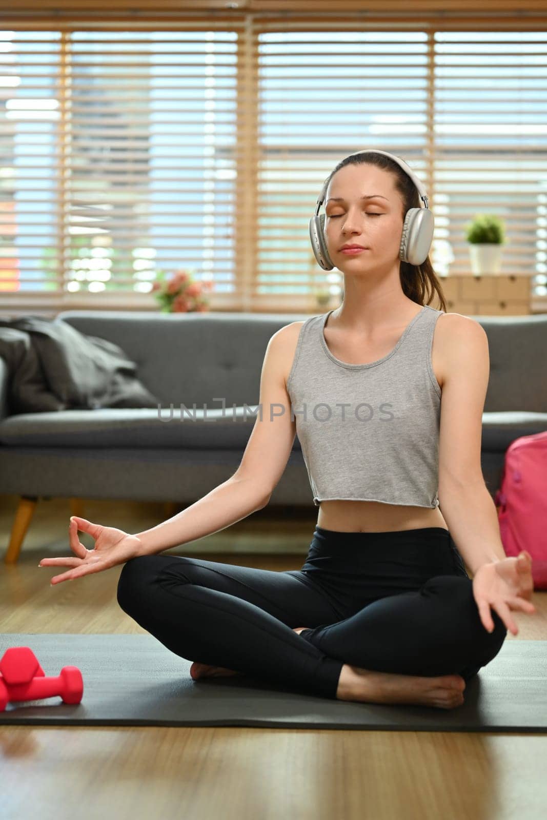 Calm young woman sitting in lotus position, listening guide instructions of meditation online in headphone.