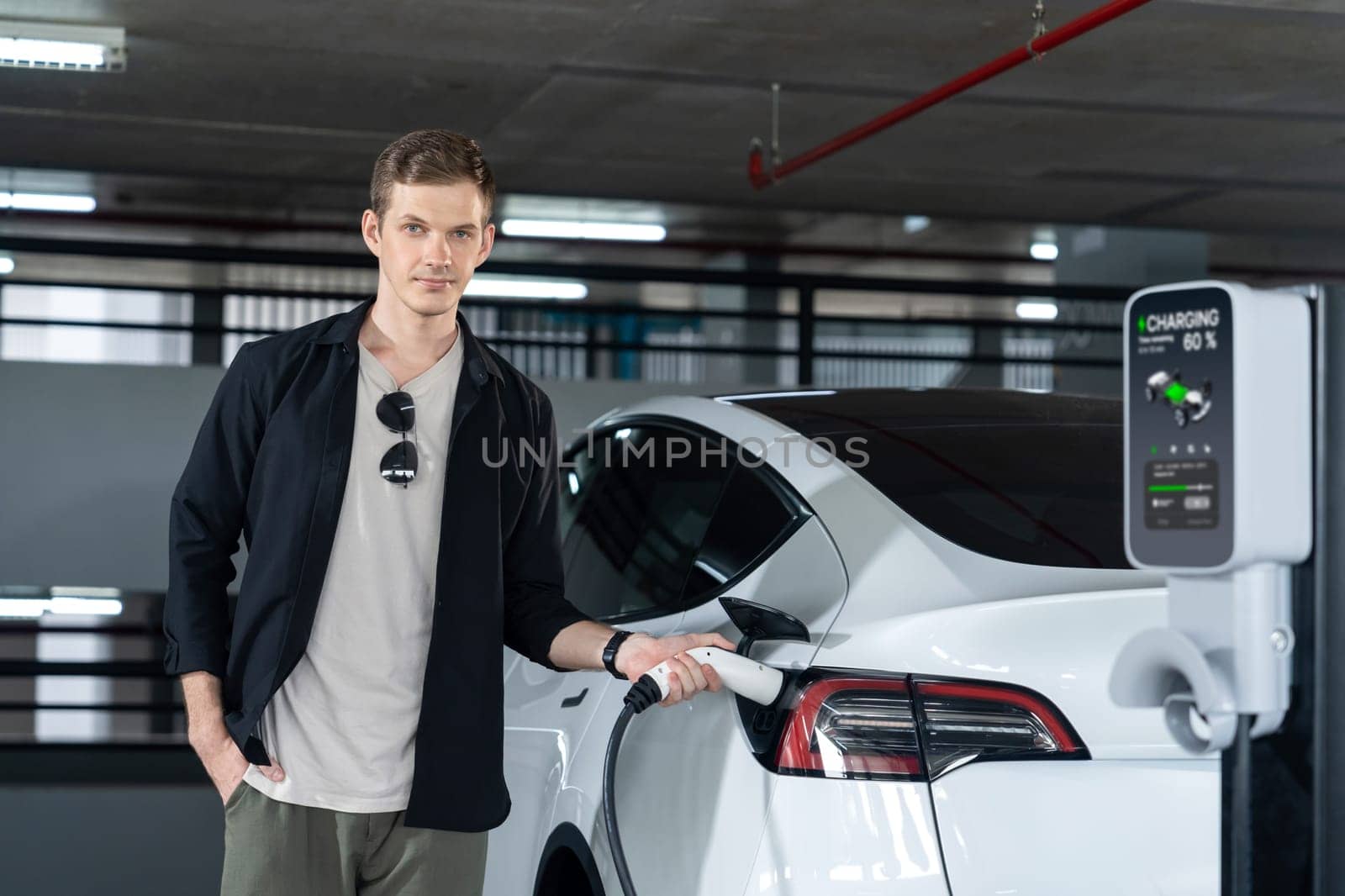 Young man travel with EV electric car to shopping center parking lot charging in downtown city showing urban sustainability lifestyle by green clean rechargeable energy of electric vehicle innards