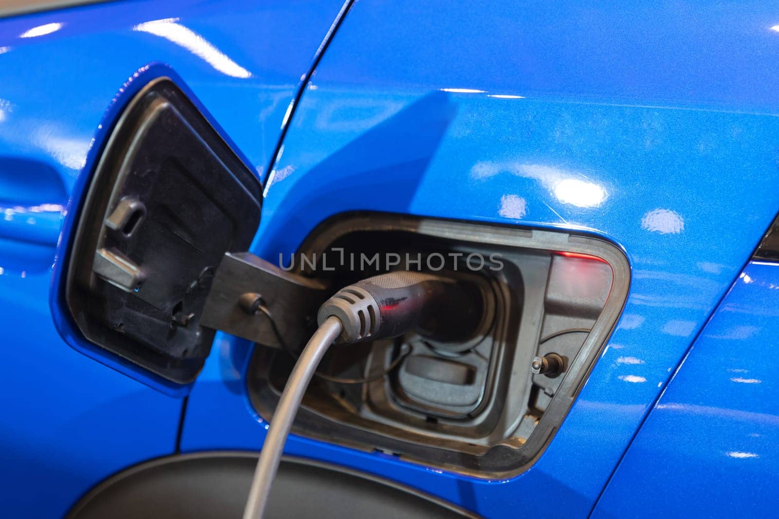 A blue car with an electric charger hooked up to it