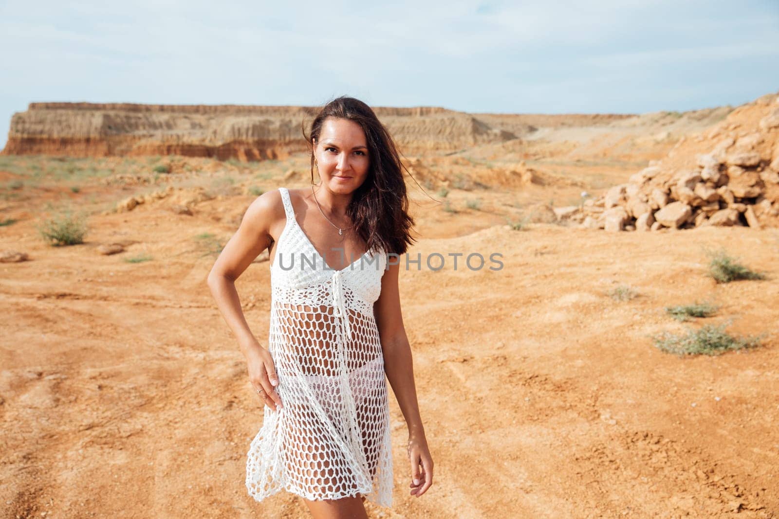 a woman in white clothes stands in a sandy locality