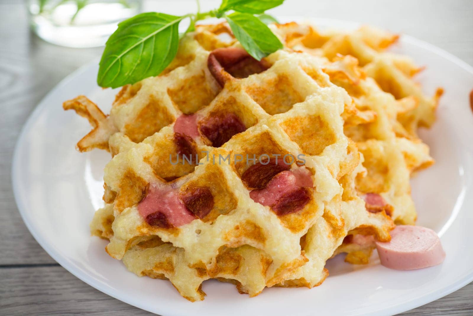 cooked fried potato waffles with sausage stuffing inside, in a plate on a wooden table.
