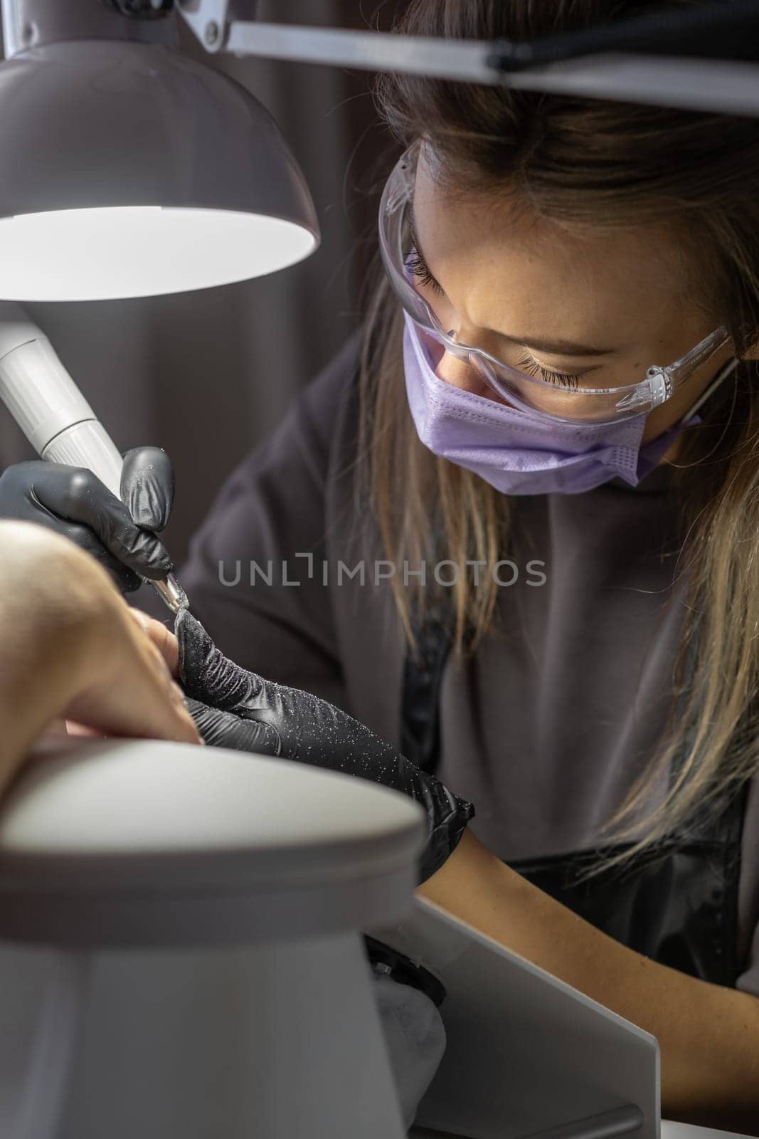 Manicurist at work. Professional manicurist removes old worn nail design from nails of client using modern electric drill. Preparing fingernails for making fresh manicure and applying new nail design