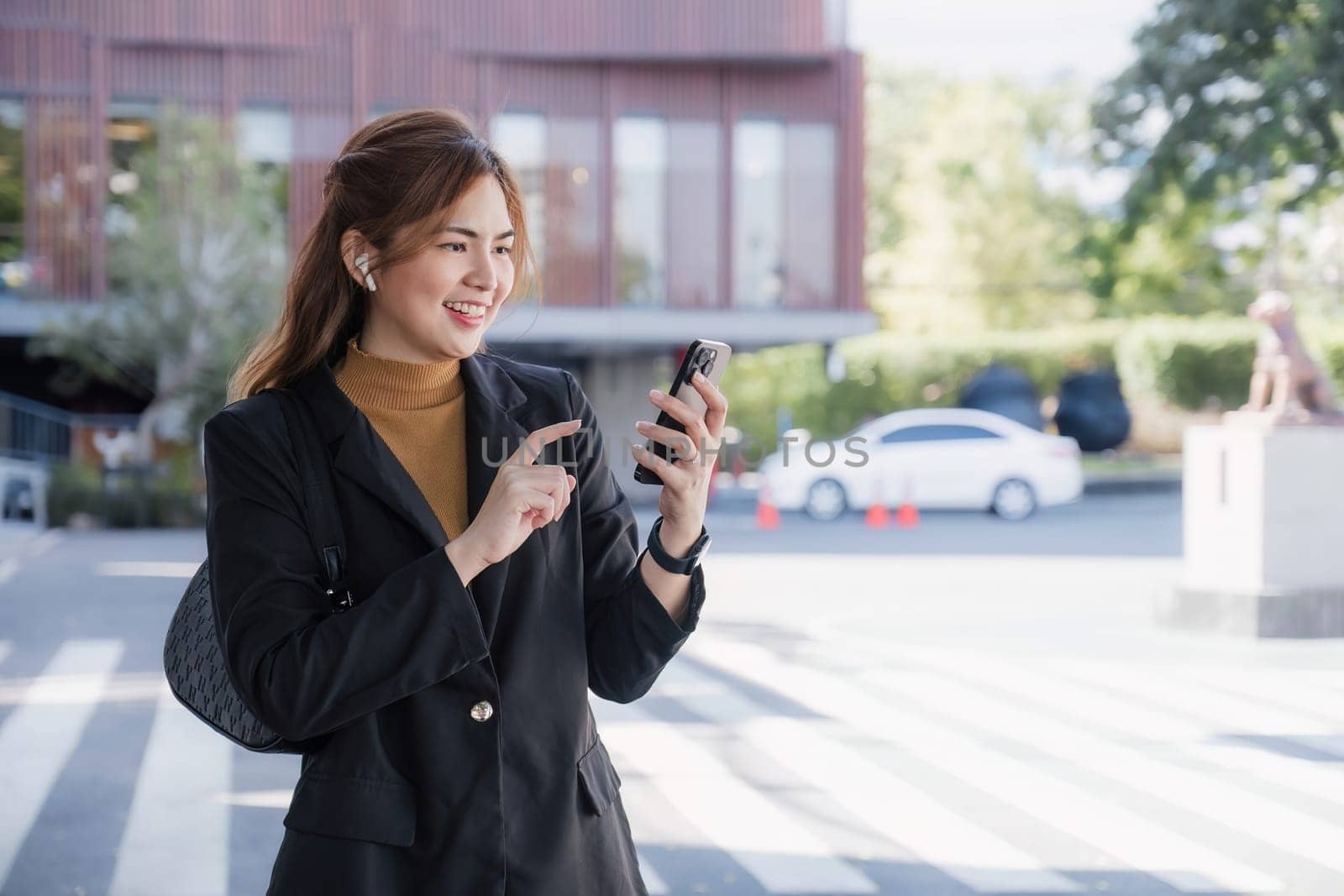 Smiling Asian businesswoman wearing a suit stands tall in the city using an application on her mobile phone. Read news on your smartphone fast connection Check outdoor mobile apps.