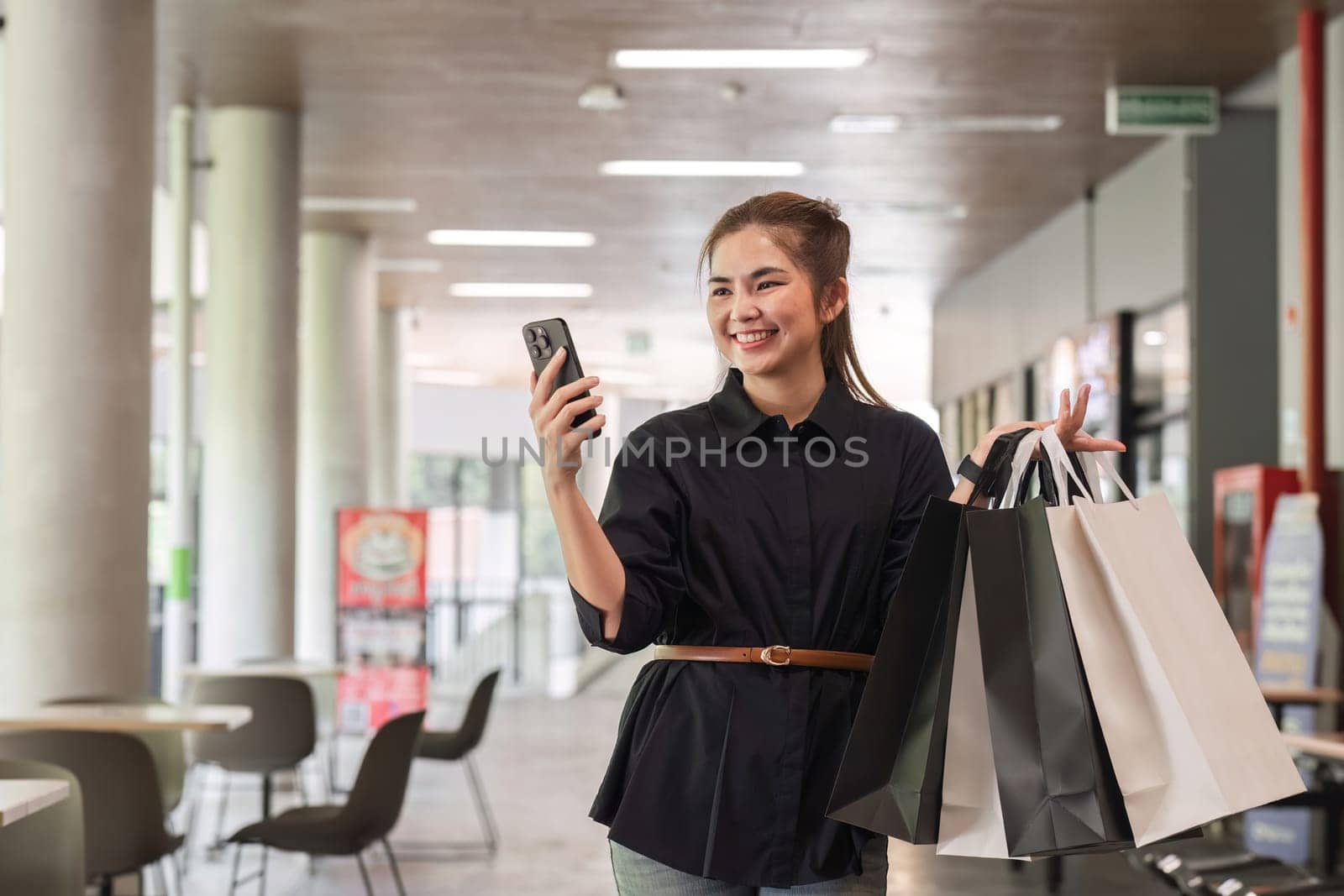 Asian woman using smartphone and looking away while enjoying a day shopping. Black Friday sale and discount. Buying clothes presents for holidays by wichayada
