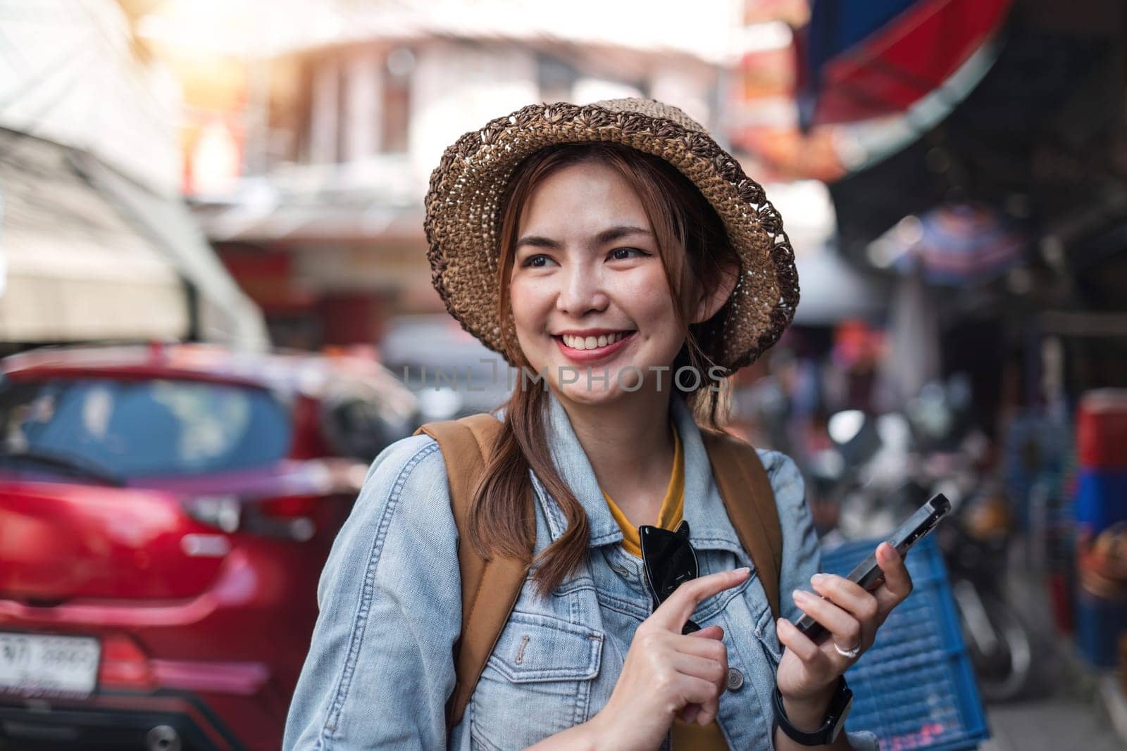 Young Asian tourist walking along city streets and holds a mobile phone on the pavement by wichayada