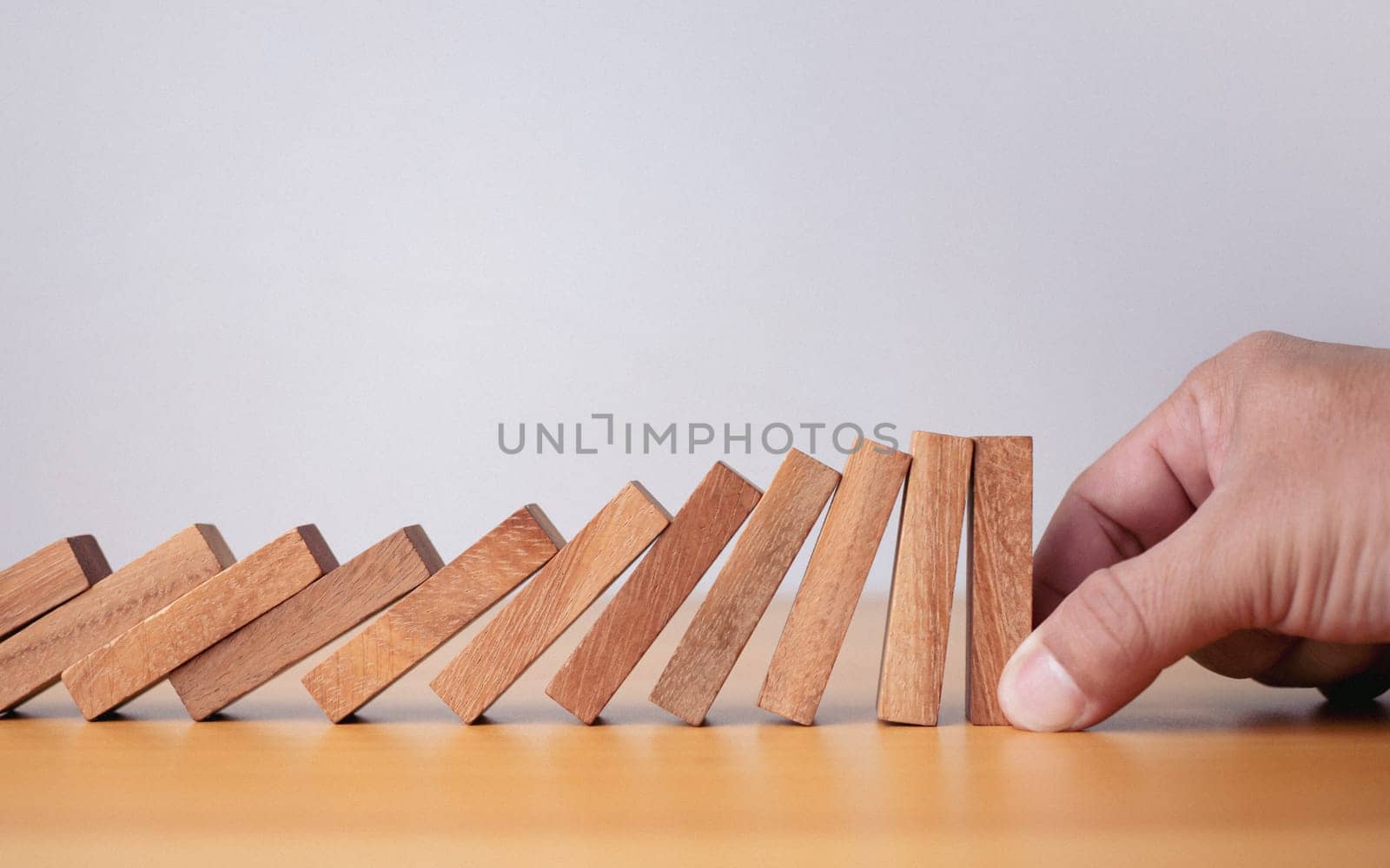 Businessman hand stopping falling blocks on table, stopping the domino effect concept for business solution, strategy and successful intervention. by Unimages2527