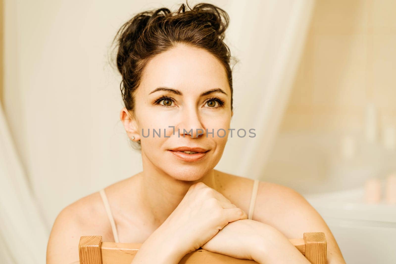 Portrait of a middle-aged woman, smiling with her arms folded in front of her face, her hair pulled up. The brunette is in a good mood. On a light background