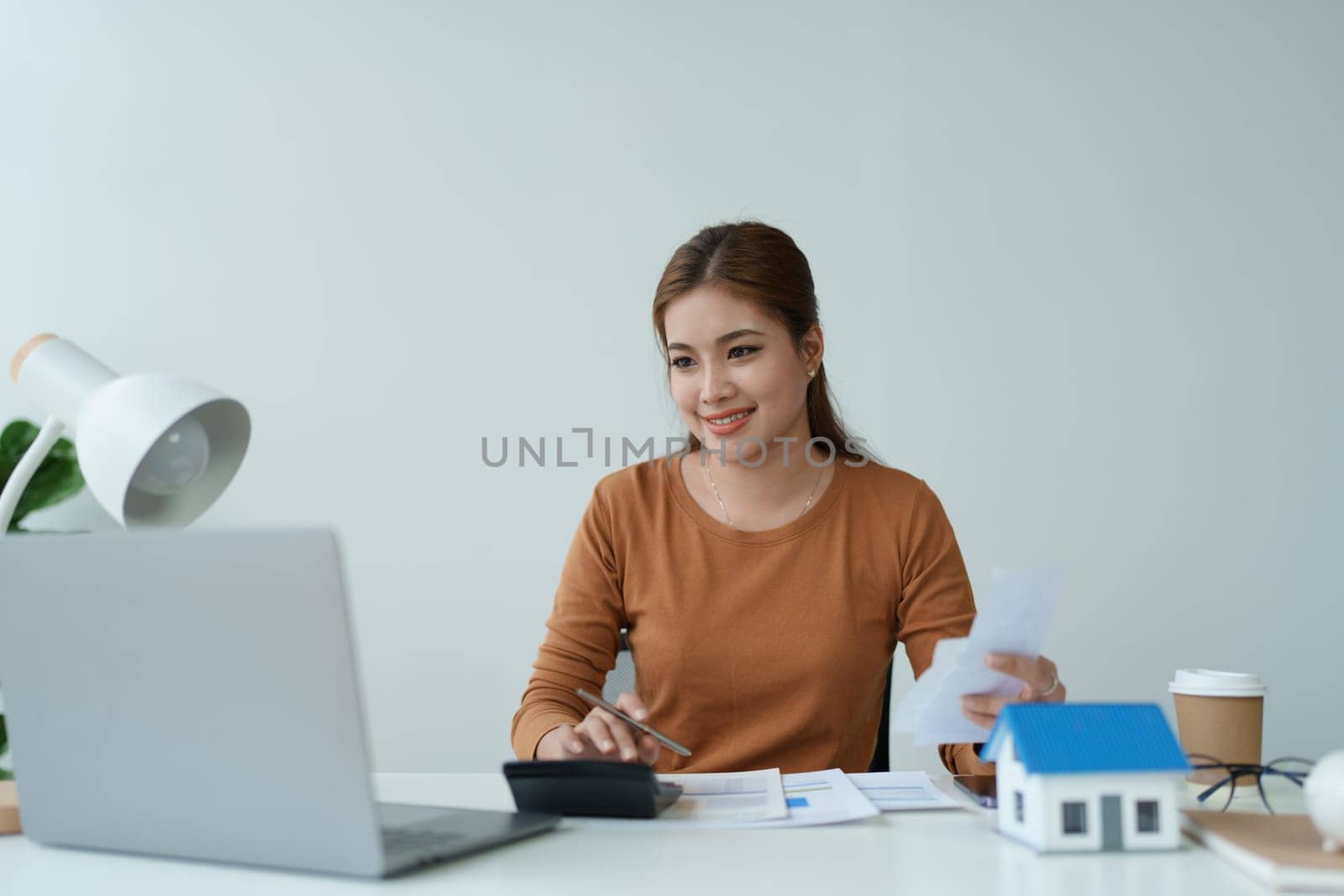 asian woman are using a calculator to calculate the loan period each month. by Manastrong