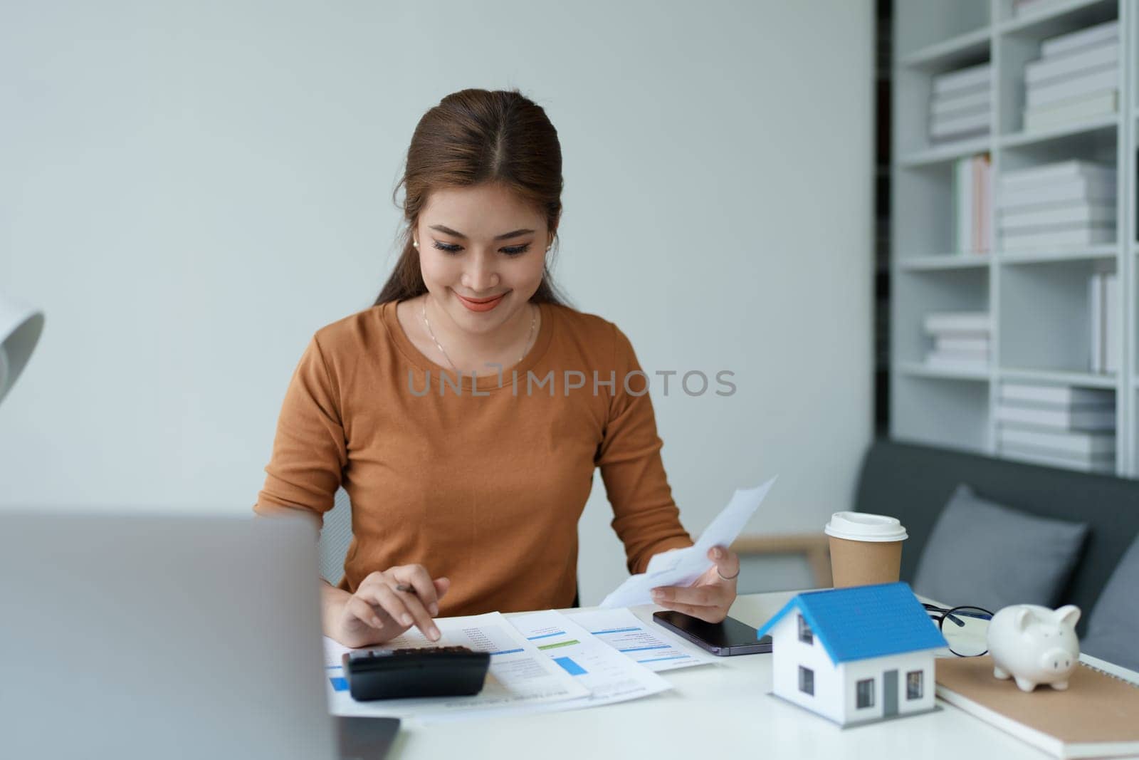 asian woman are using a calculator to calculate the loan period each month. by Manastrong