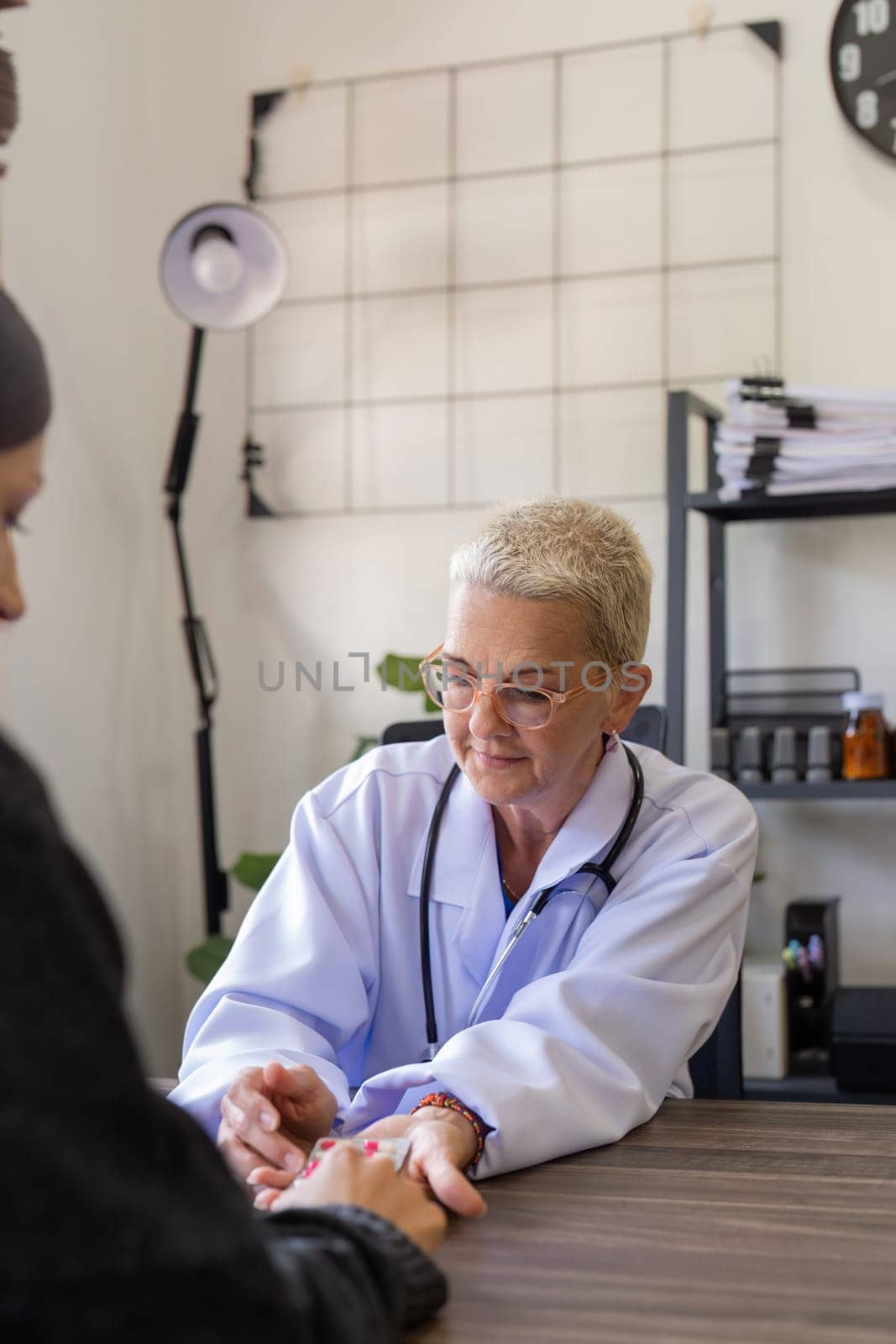 Senior woman doctor and female patient talking recommend pill medical prescription at doctor office. Hospital, medicine and healthcare by nateemee