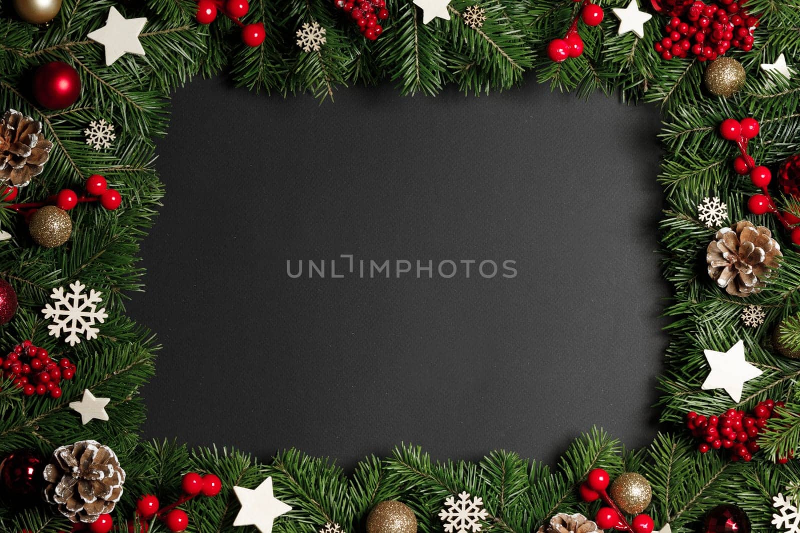 Christmas Border frame of tree branches on black background with copy space , red and wooden decor, berries, stars, cones