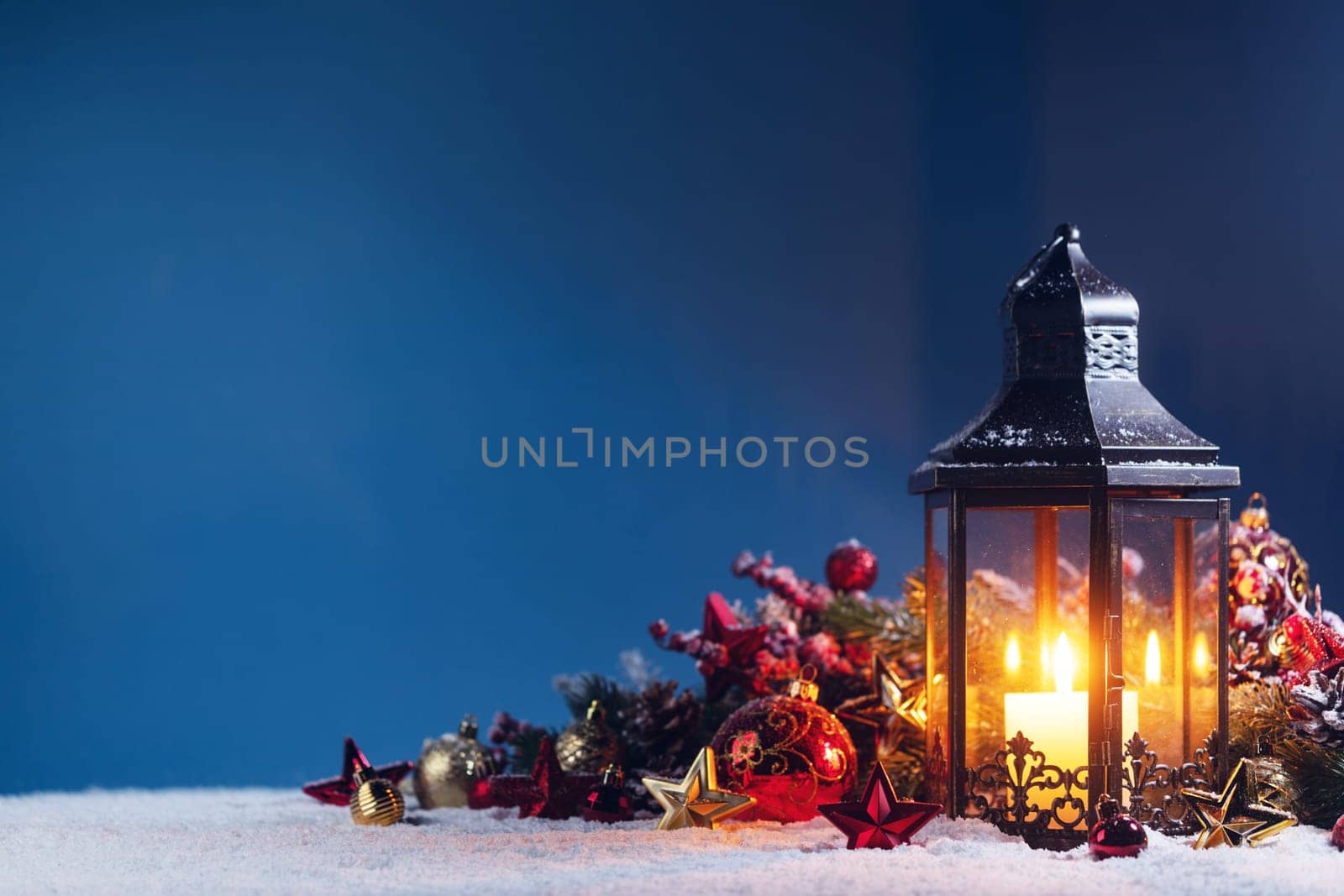 Christmas background with burning candle inside lantern and bauble decorations in snow