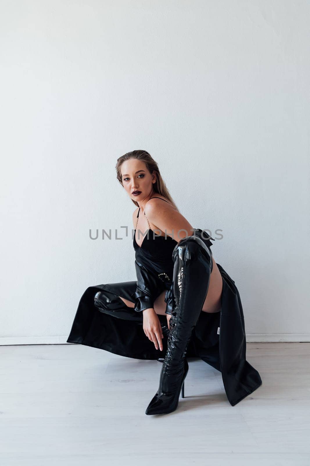 woman in a leather cloak and black clothes sits on a white background