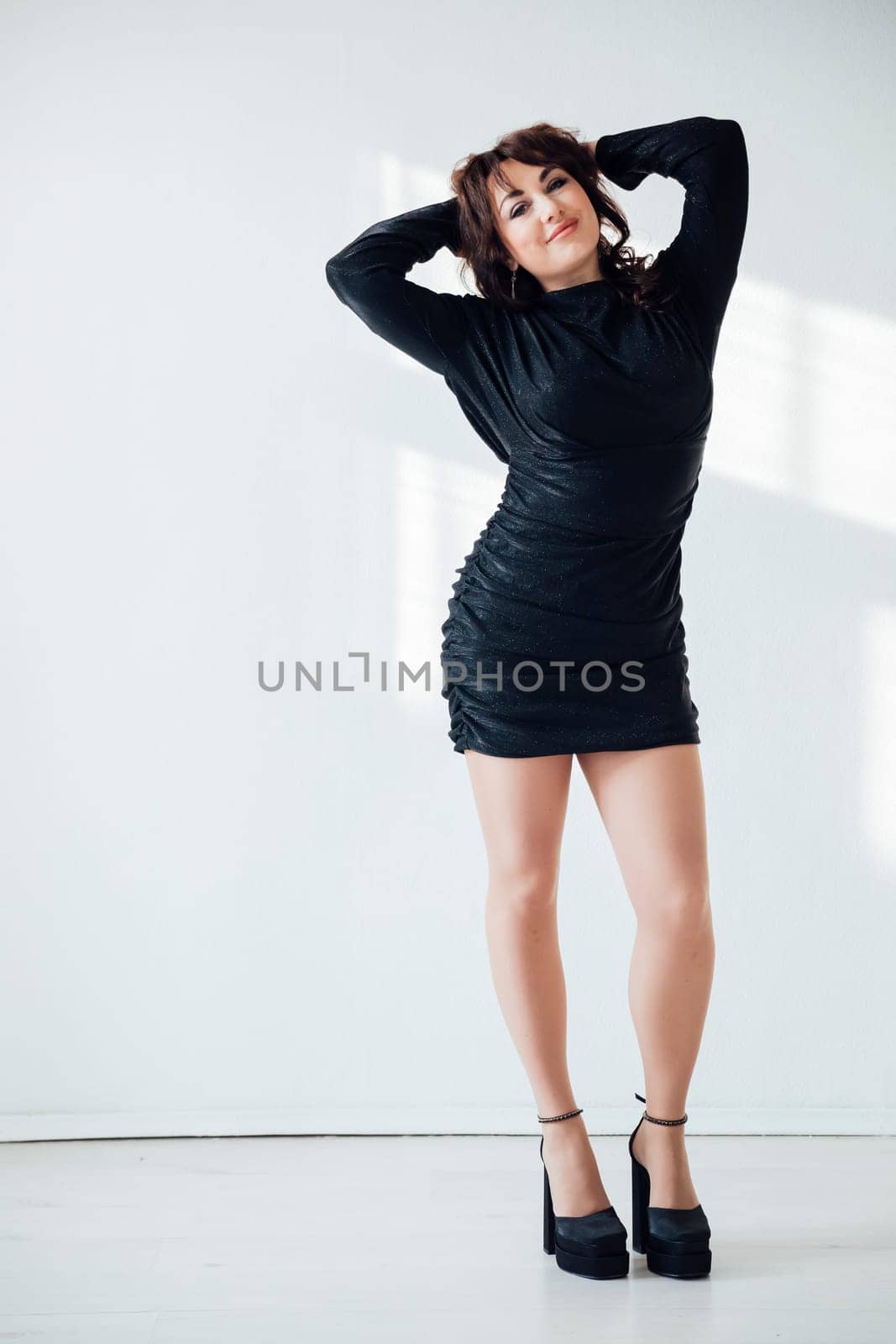 woman in a black dress stands against a white wall in the background