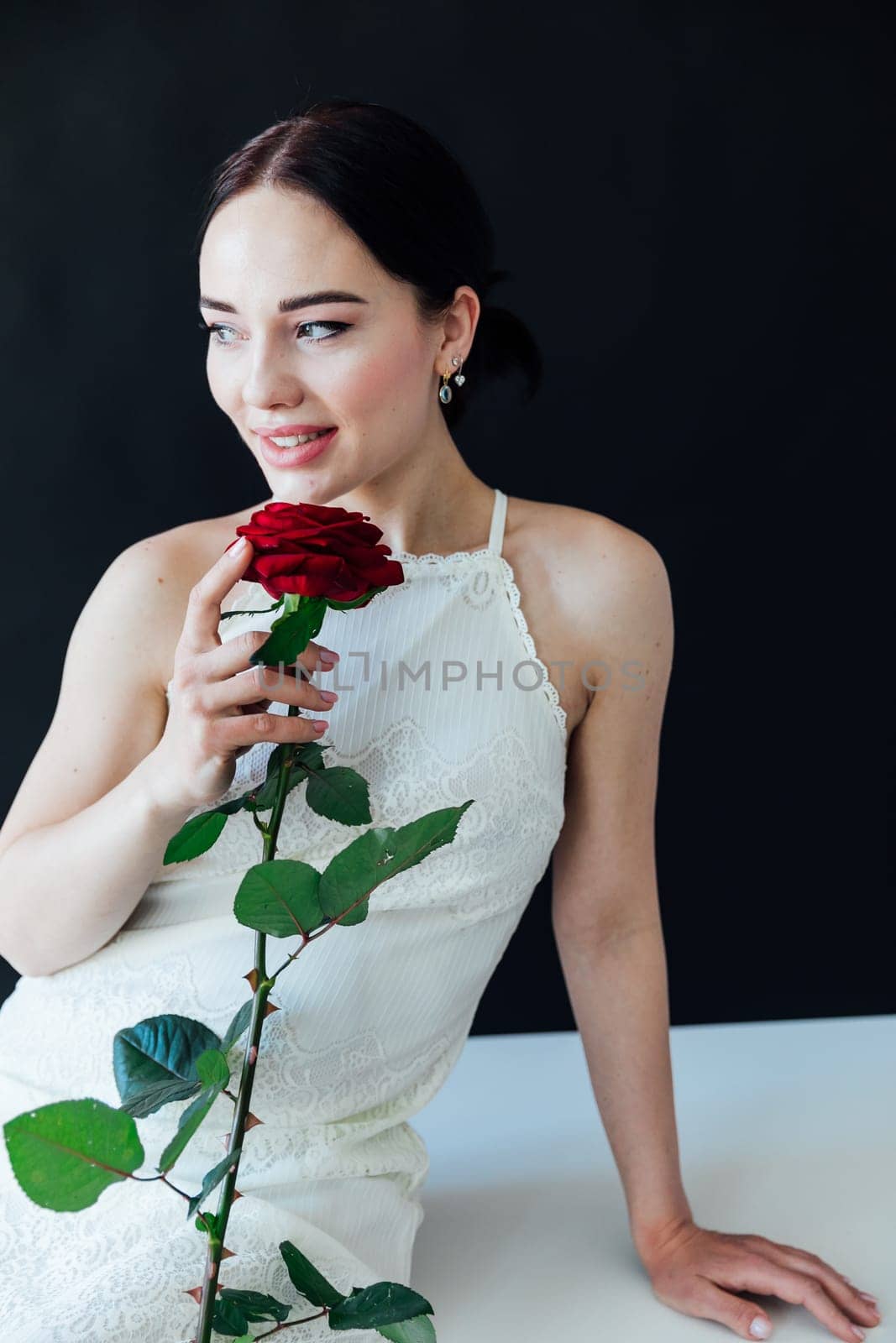 beautiful brunette in with a red rose sits near a black wall by Simakov