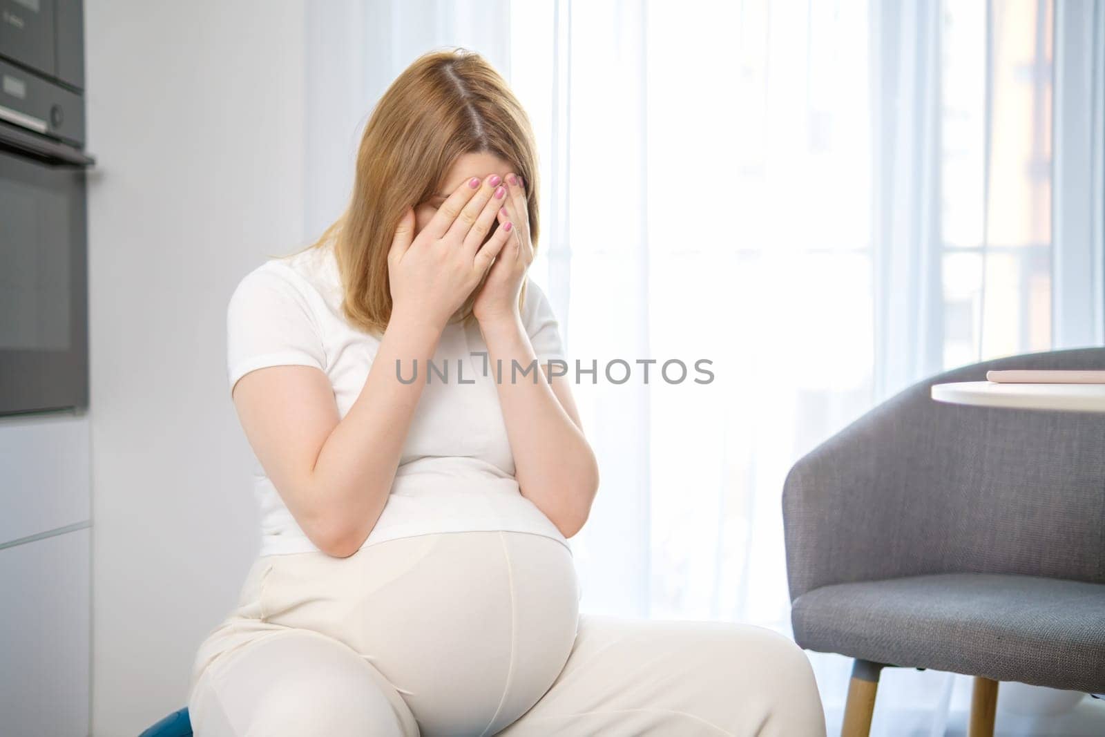 Tired pregnant woman closes her face with her hands.