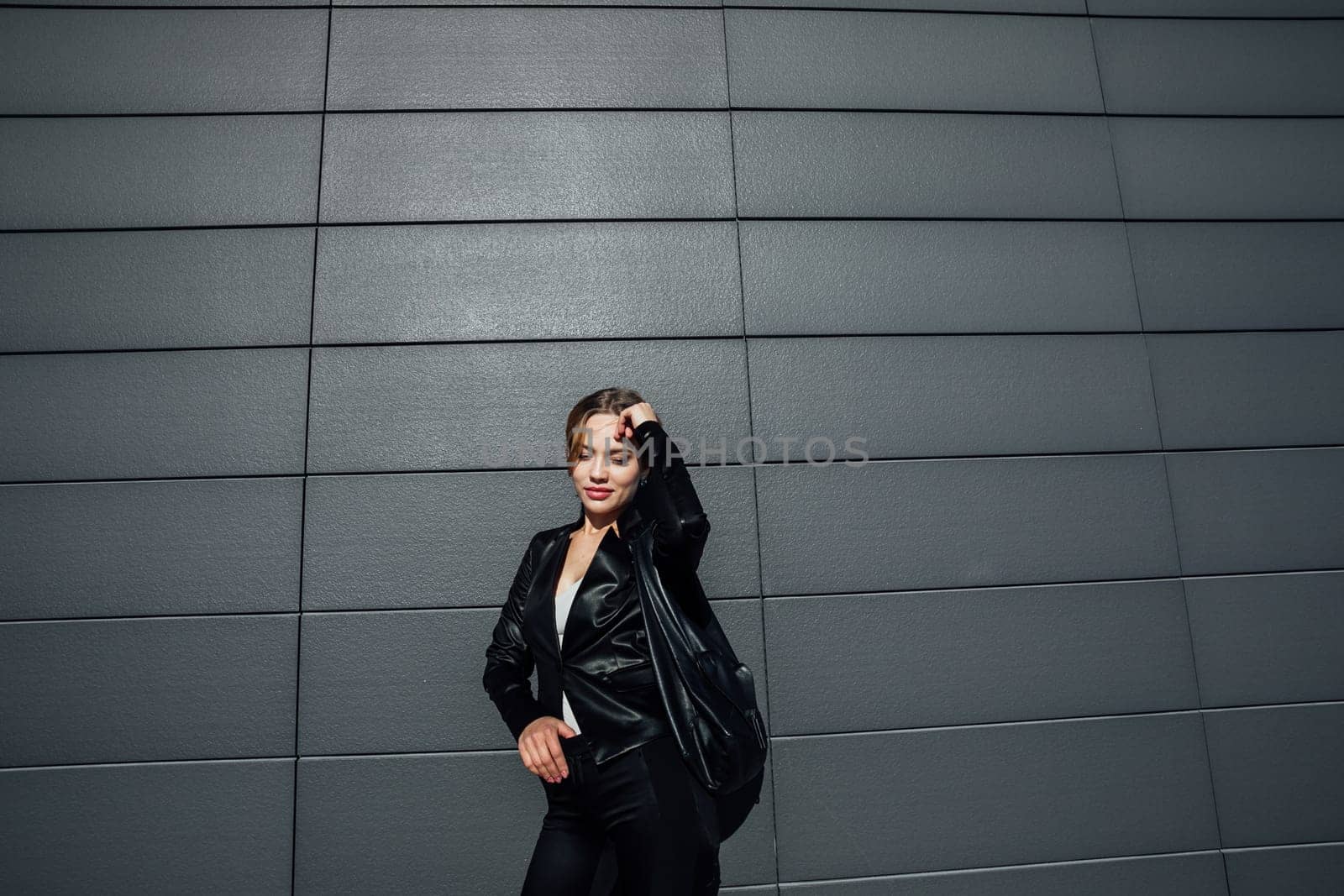 a fashionable woman in leather black clothes near the black wall of the building