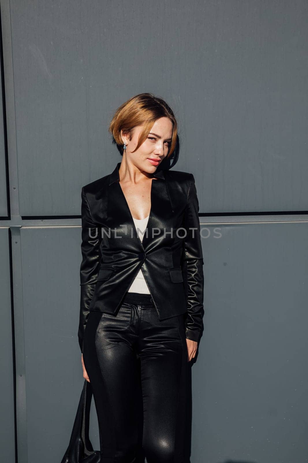 a fashionable woman in leather black clothes near the black wall of the building