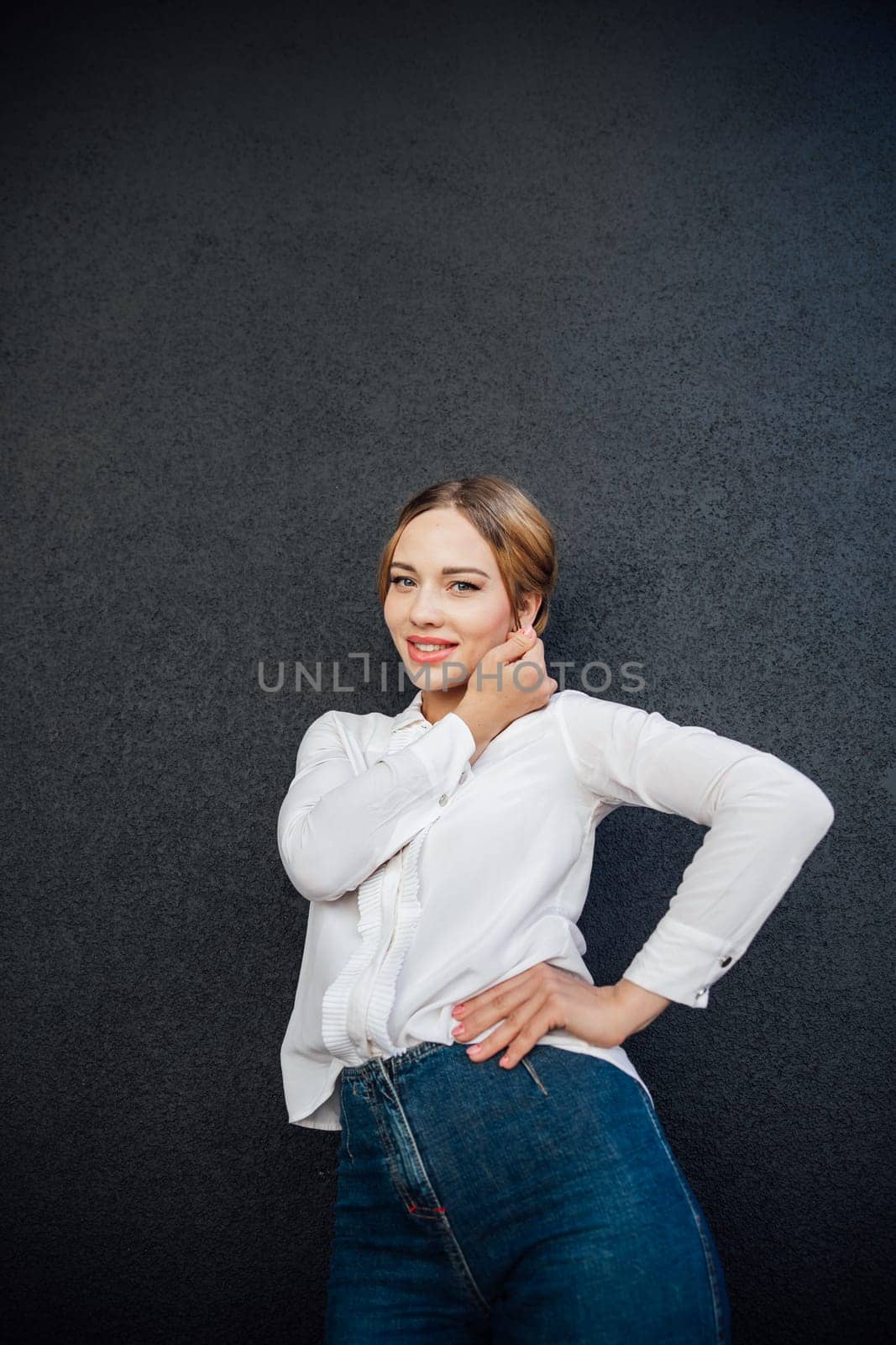 fashionable woman in jeans poses against a black wall