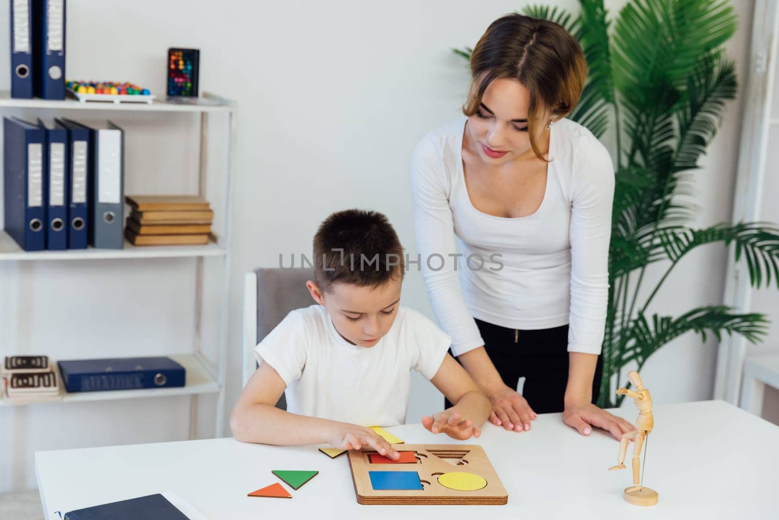 a boy with a psychologist in the office plays board games by Simakov