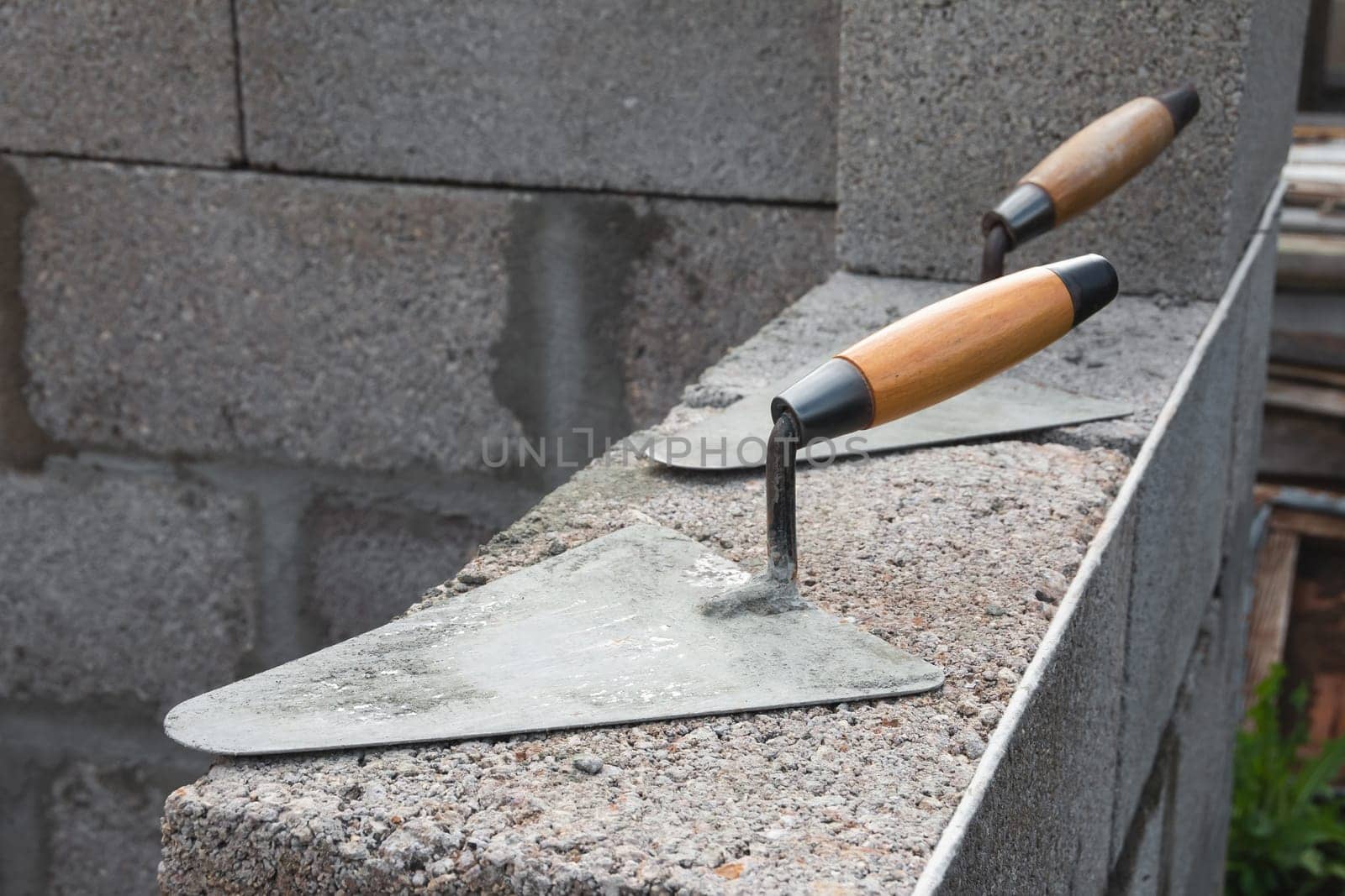 The concrete worker's trowels lie on a cinder block construction stone. It is used for bricklaying, as well as for measuring and applying cement mortar