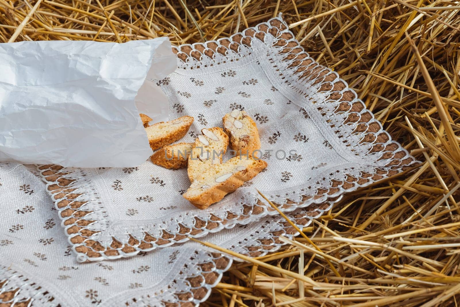 Almond cookies crackers with pieces of nuts fell out of a paper bag on a napkin lying on the straw by ElenaNEL