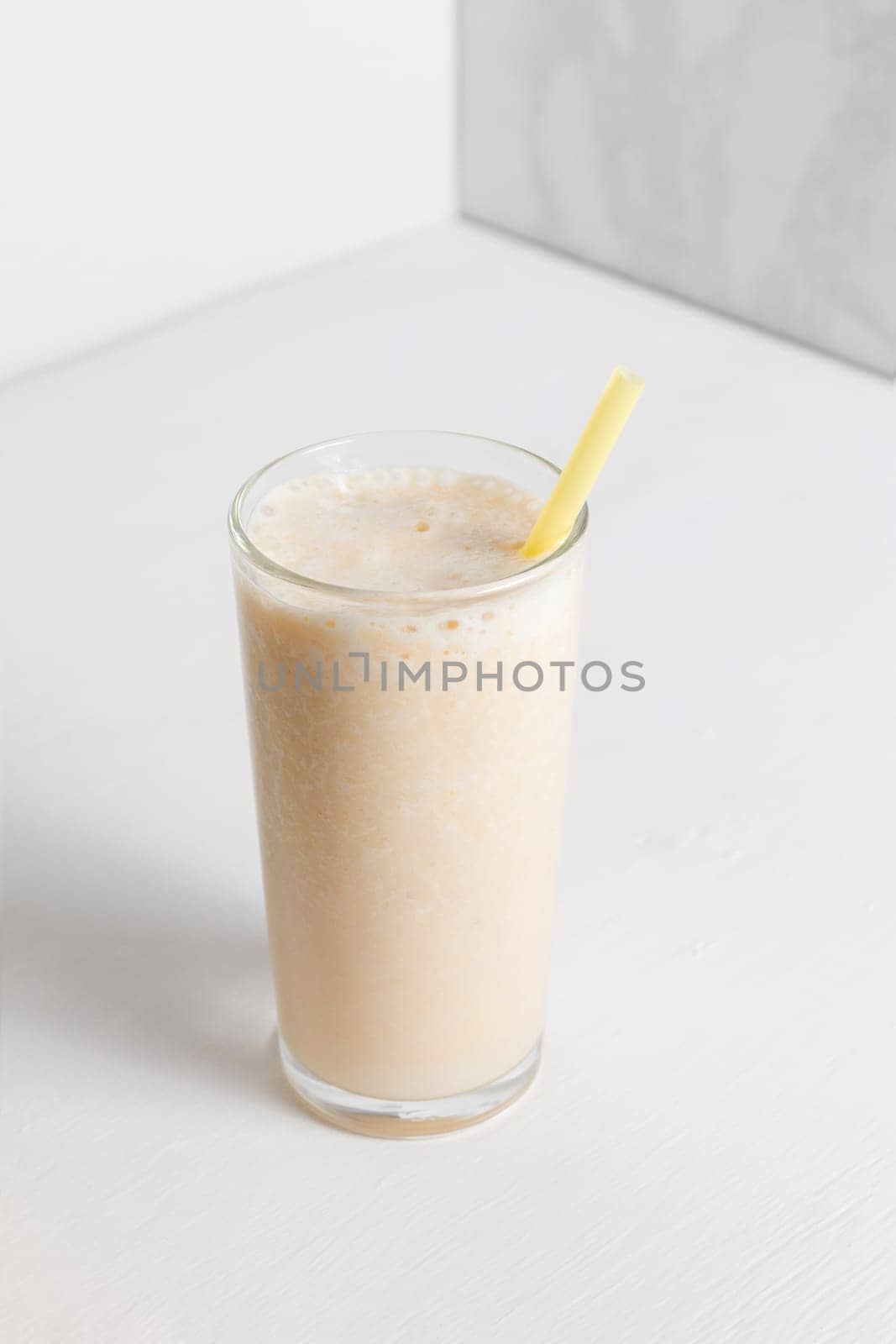 Milkshake with banana in a high transparent glass on a white background. A healthy drink for a diet