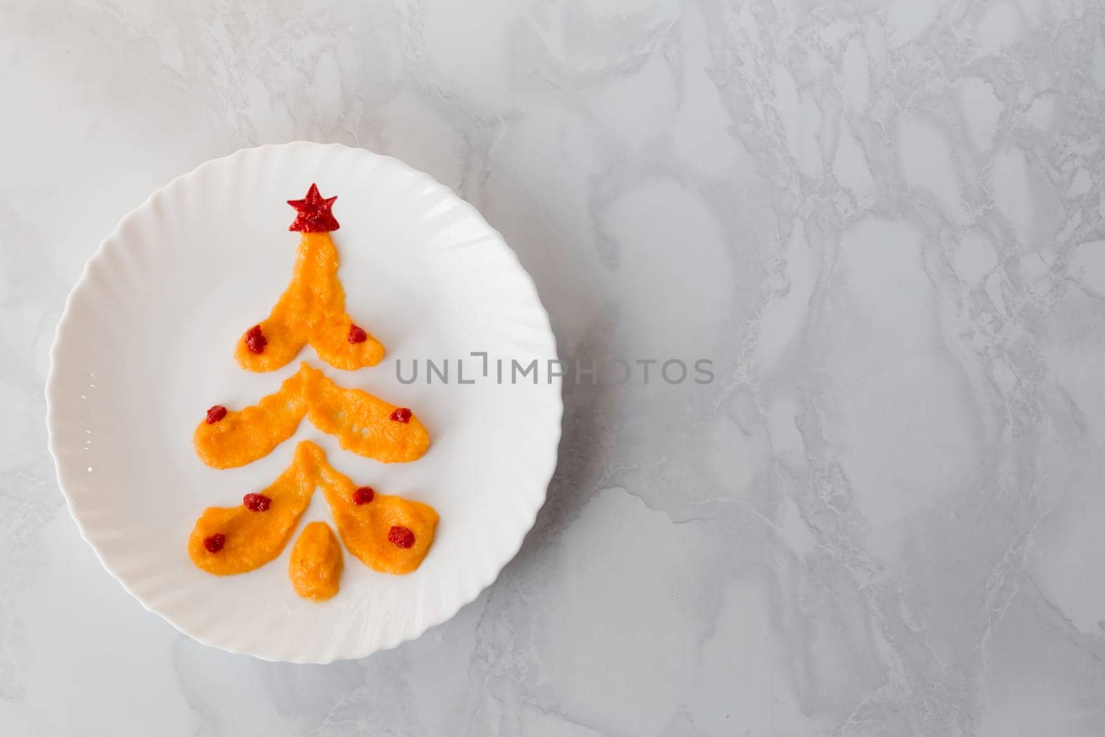 Squash caviar on a white plate in the shape of a Christmas tree decorated with balloons and a ketchup star. Alternative Christmas tree made of food with copy space