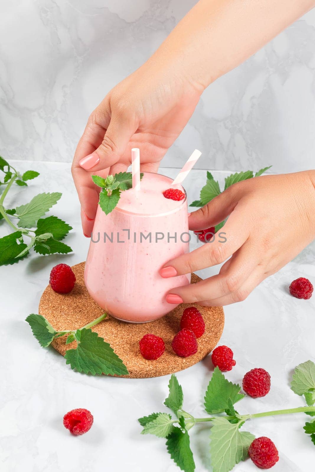 Women's hands put a milkshake with raspberries in a glass glass on the table