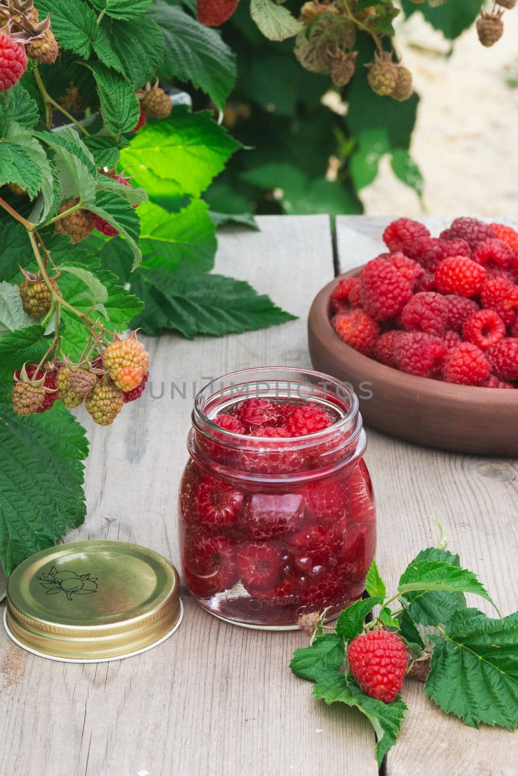 Raspberry berry fresh in a clay plate and in a jar for preservation on a wooden table