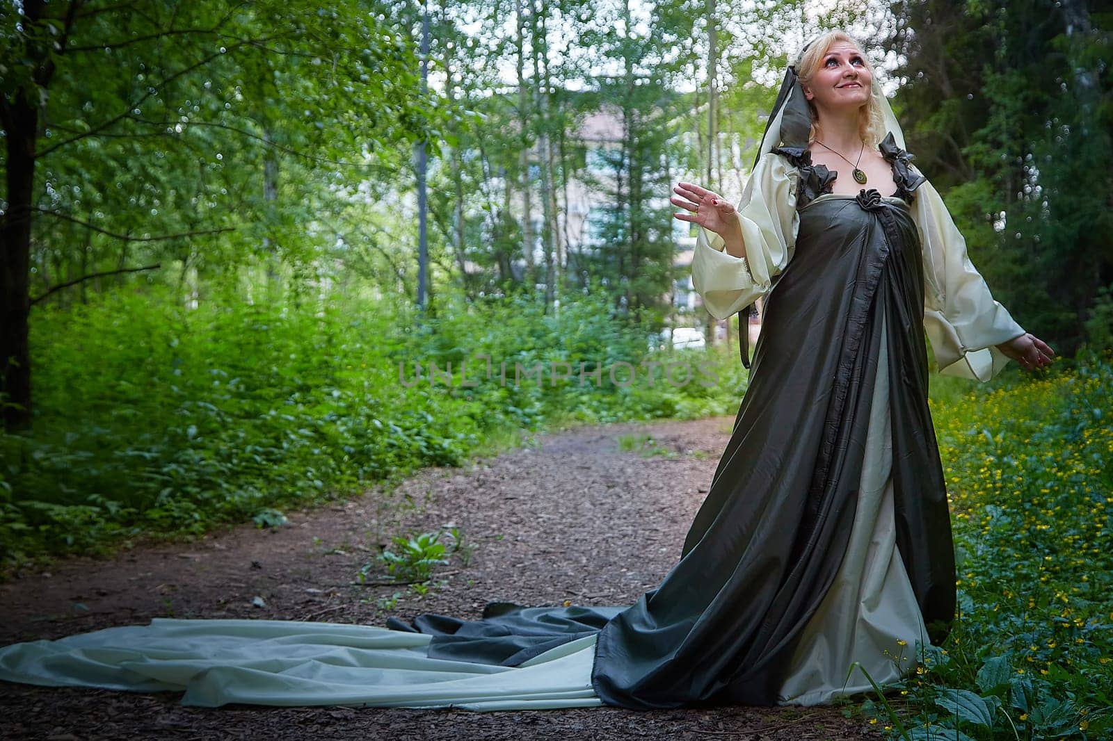 Adult mature woman 40-60 in a green long fairy dress in forest. Photo shoot in style of dryad and queen of nature. Fairy in beautiful green summer forest. Concept of caring for nature