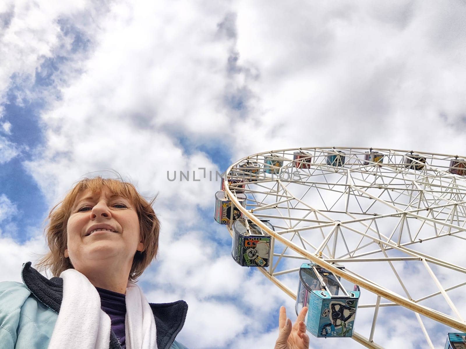 Relaxed mature caucasian female making selfie outside near big Ferris wheel. Positive senior woman against city street. Adult middle agged girl Blogger taking photo for internet