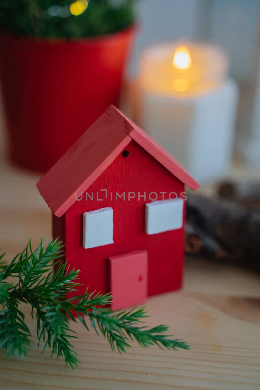 Wooden red house to decorate the house for the Christmas holidays. Wooden toy for the Christmas tree. A candle in a jar is burning in the background. Juniper branches. A product handmade.